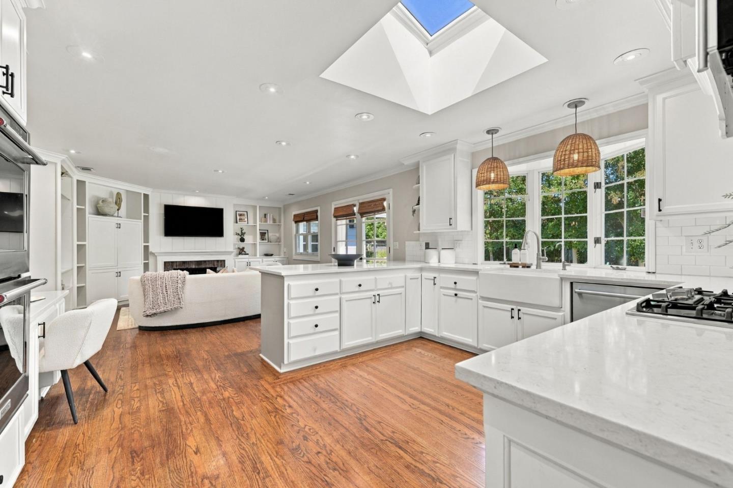 Bright white kitchen with a large island, skylight, woven pendant lights, and warm wood floors.