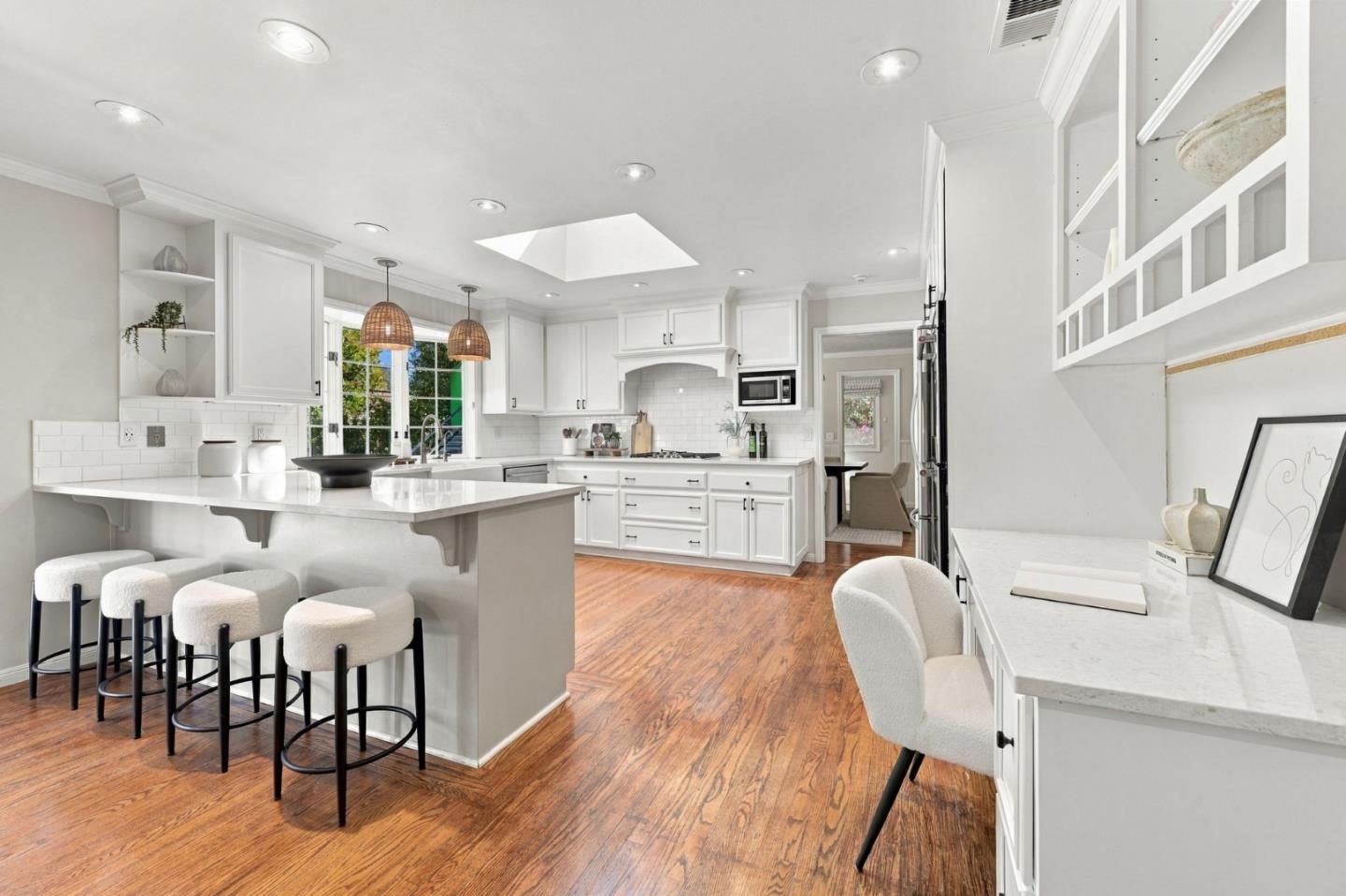 Bright white kitchen with a large island, four stools, hardwood floors, and a skylight.