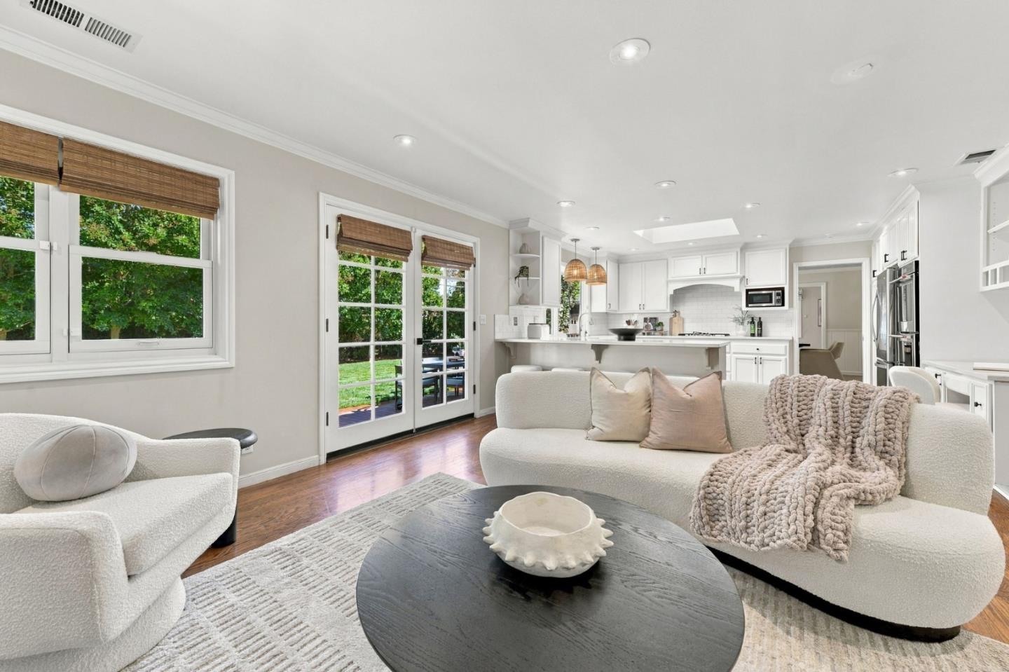 Staged living room with cream seating, a dark round coffee table, and French doors opening to the garden.