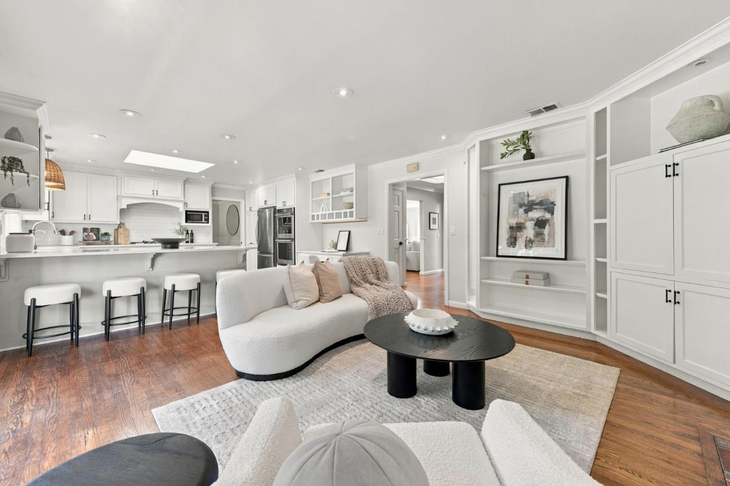 Open-plan kitchen and living room with white cabinetry, built-ins, and a curved sofa.