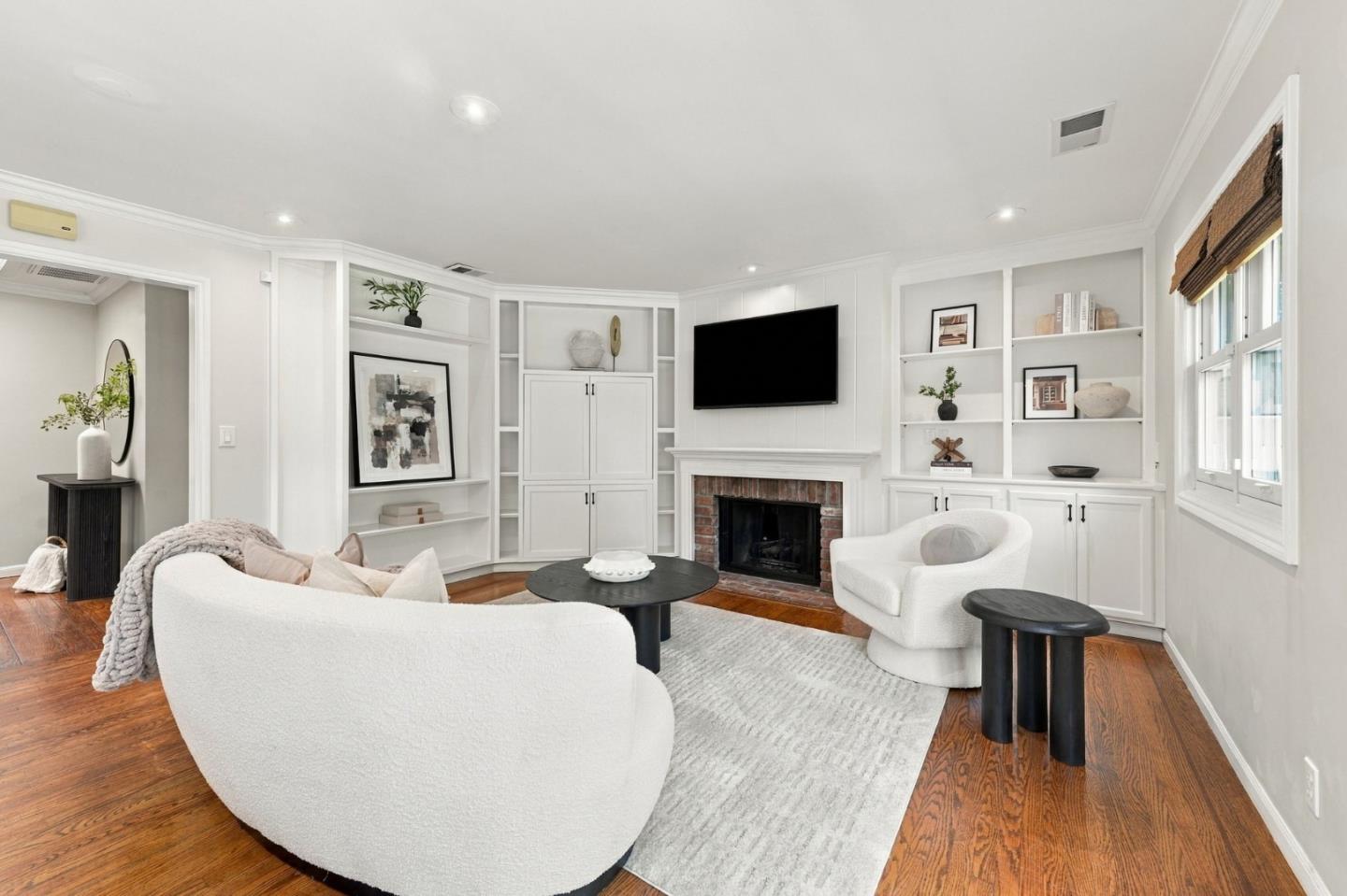 Living room with a brick fireplace, white built-ins, curved seating, and hardwood floors.