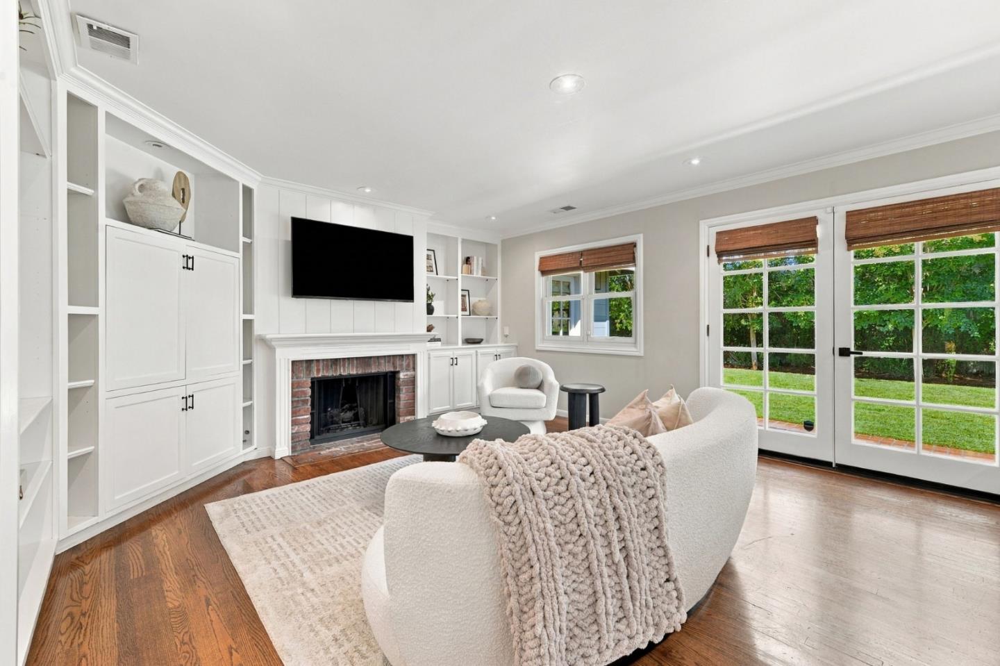 Living room with white built-ins around a brick fireplace and French doors overlooking a garden.