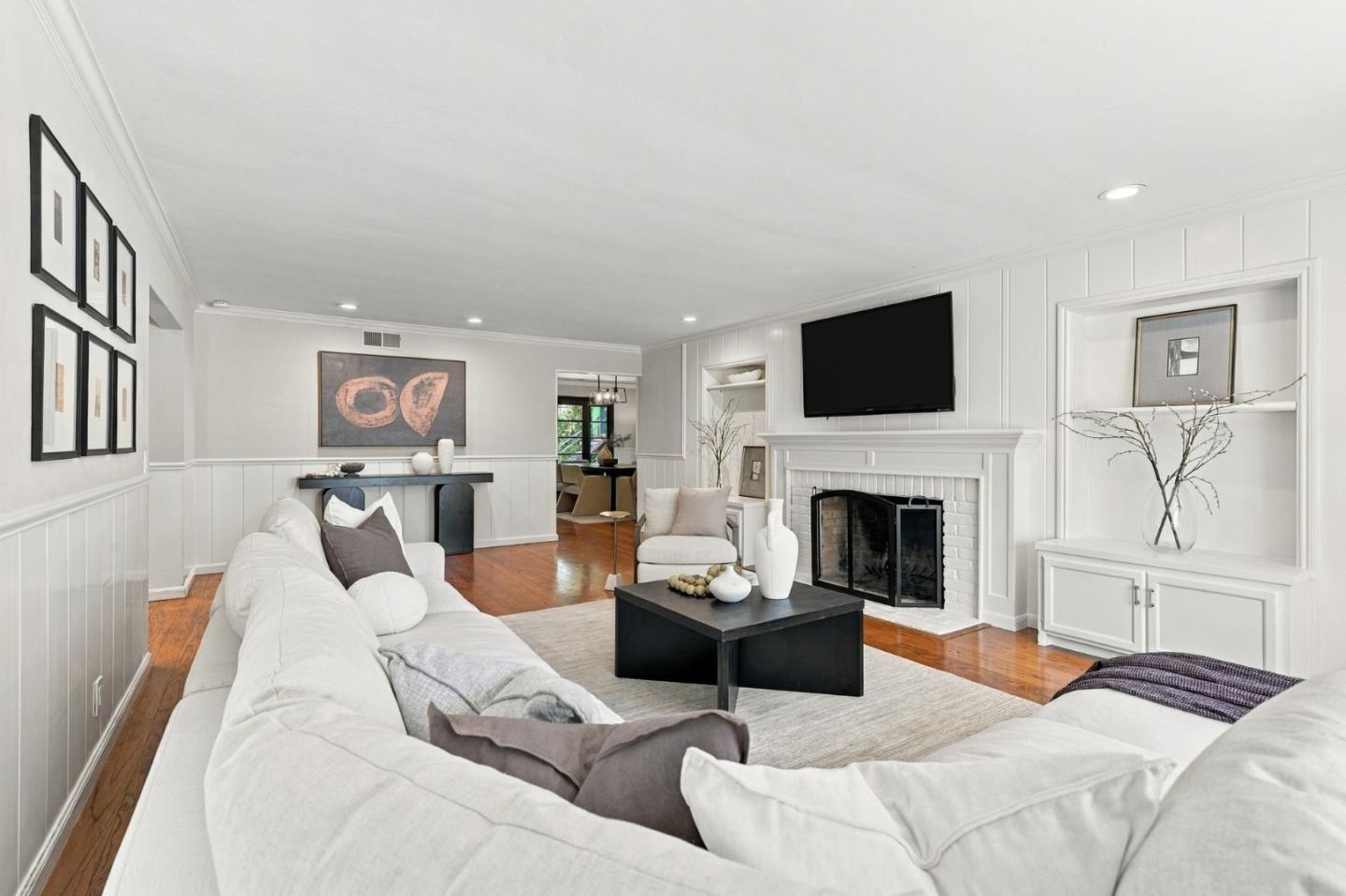 Living room with a white sofa, hardwood floors, and a white brick fireplace beneath a television.