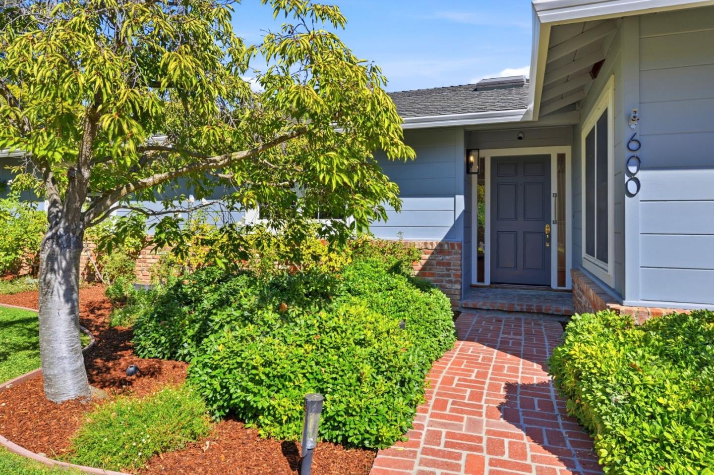 Home entrance with a dark double door, brick walkway, and leafy landscaping.