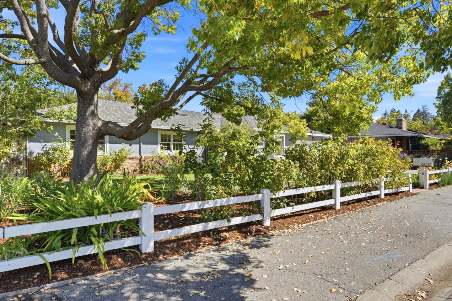 Single-story home behind a white fence and mature tree, with landscaped garden and address marker 600.