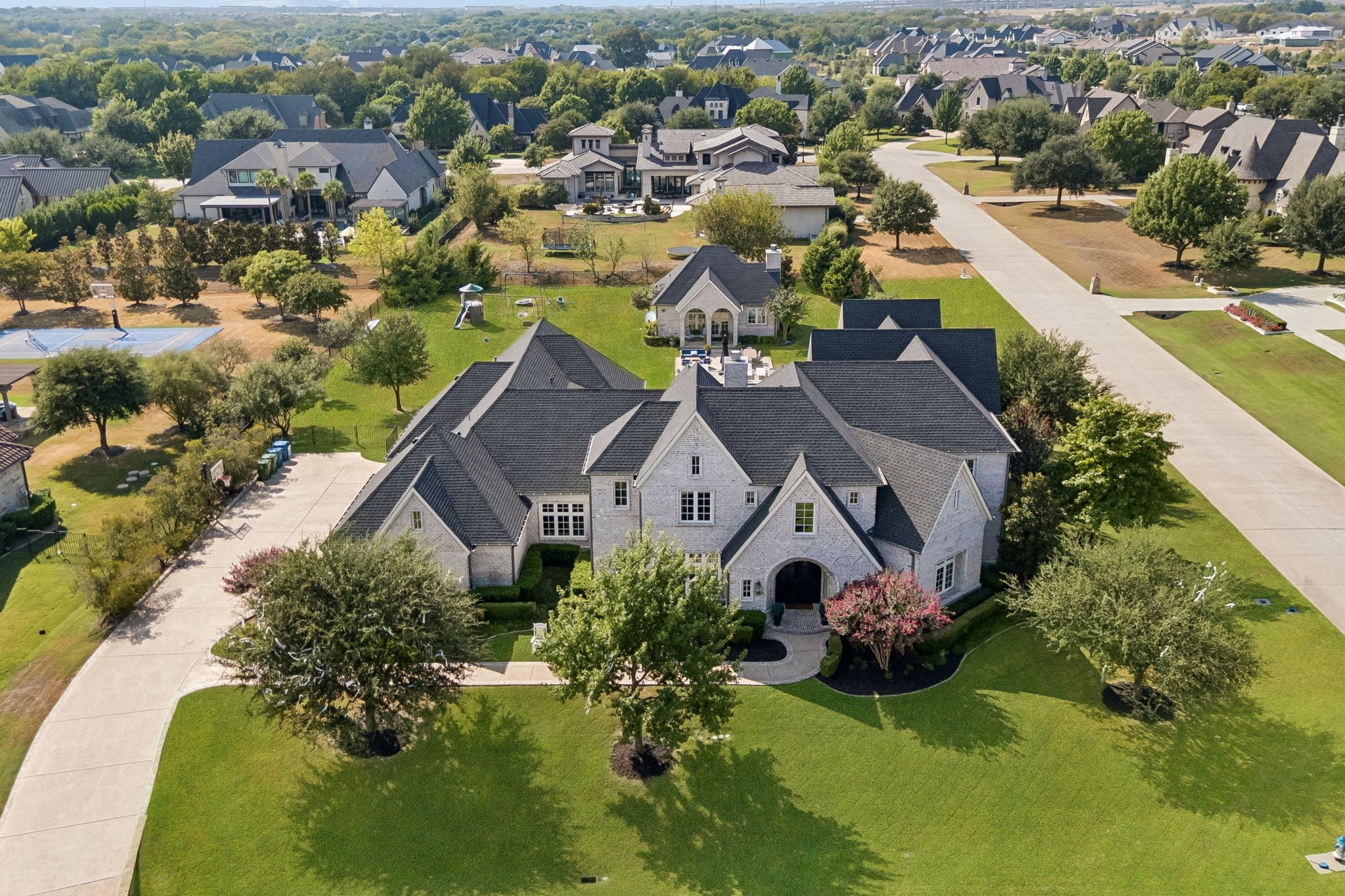 Aerial view of a large stone house with a dark roof, landscaped lawn, and curved driveway.