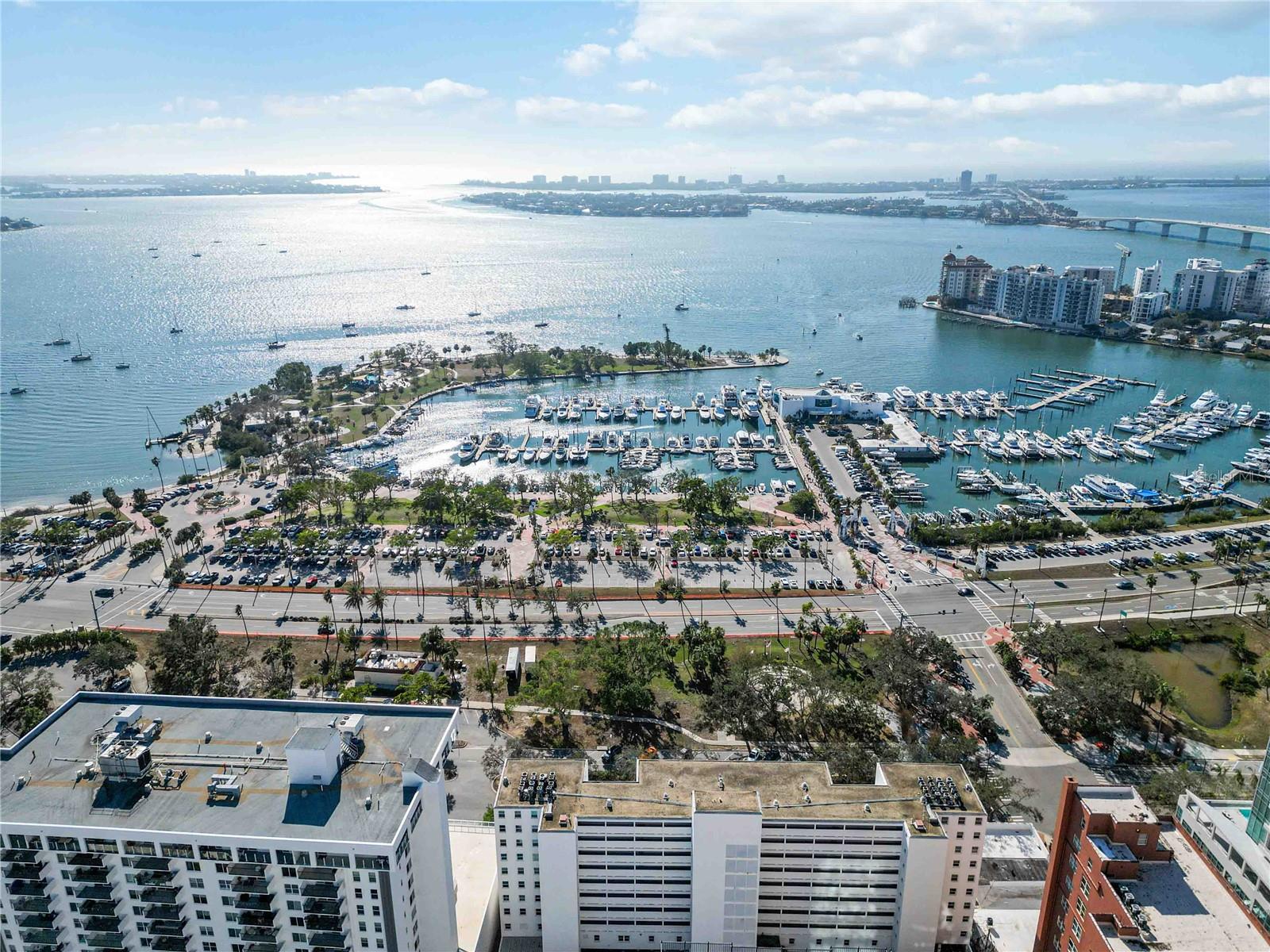 Aerial view of Sarasota Bay marina, with boats, waterfront buildings, and a bridge.
