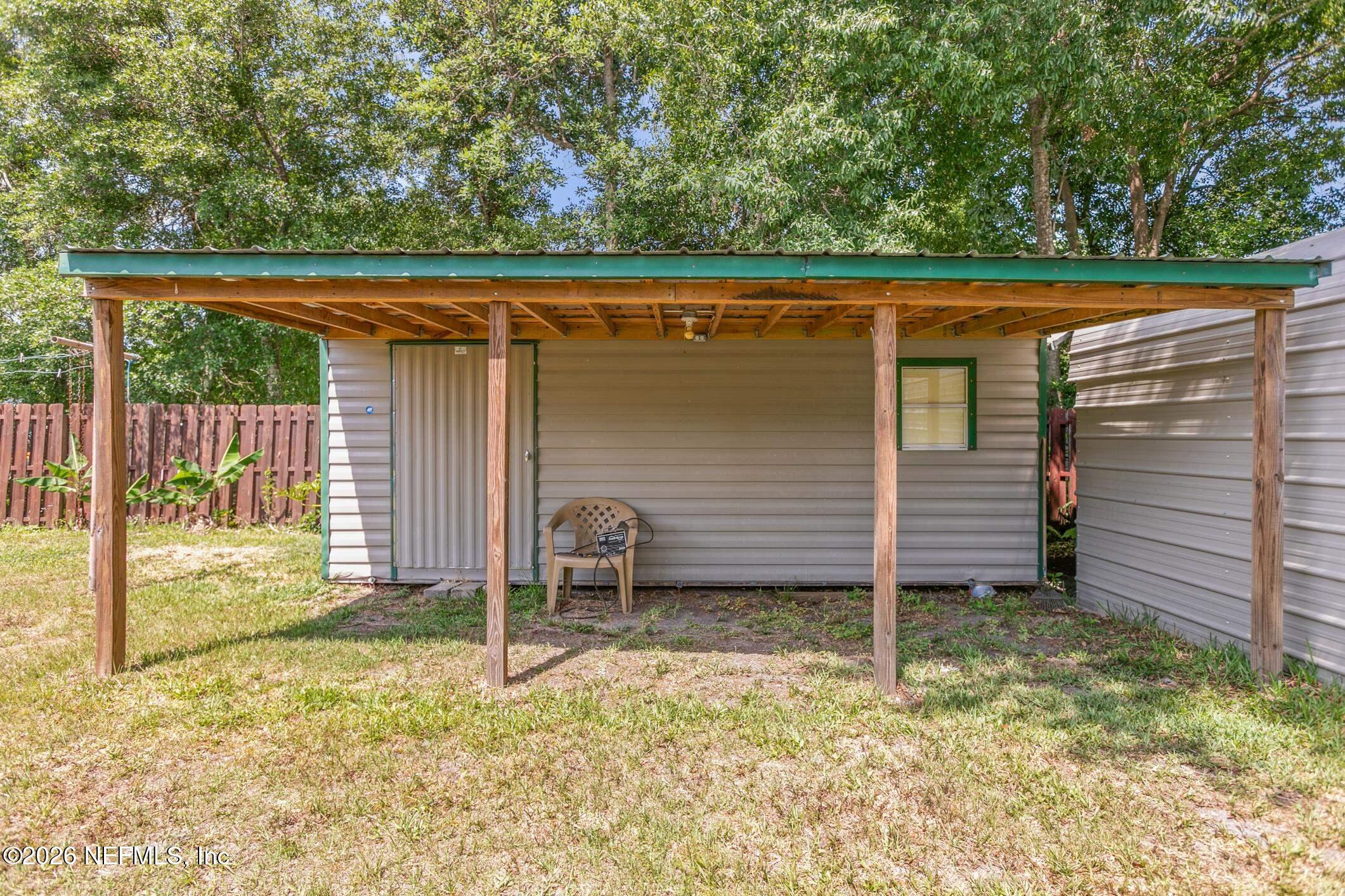 Home’s rear exterior with a broad wooden covered patio and green metal roof.