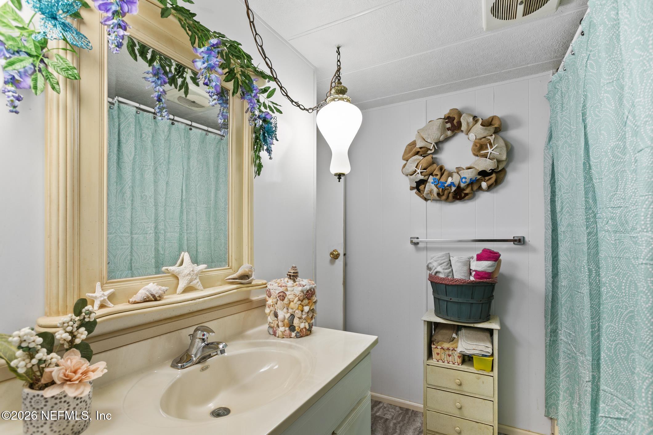 Bathroom with an aqua shower curtain, seashell accents, and a cream vanity.