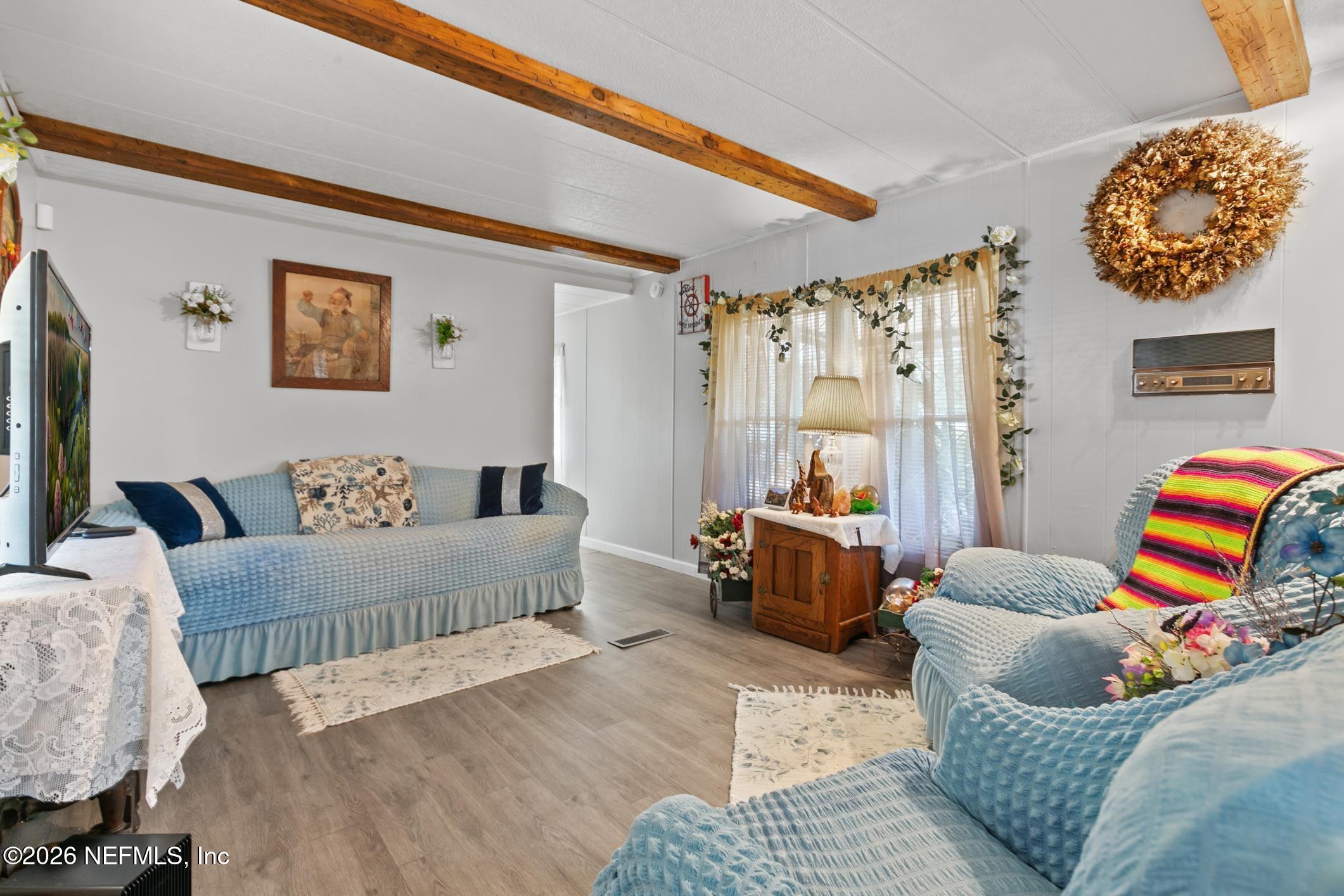 Living room with blue upholstered seating, exposed wood ceiling beams, and a curtained window.