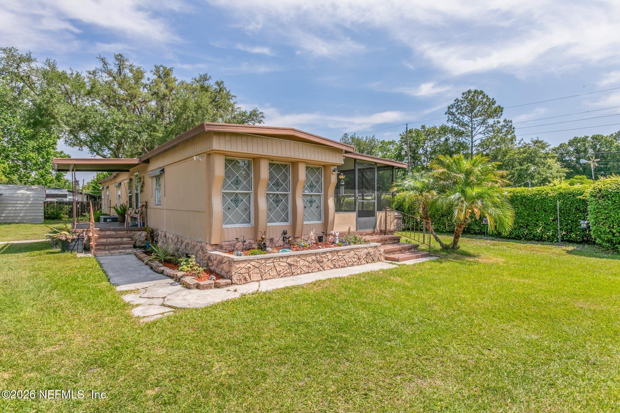 Tan single-story home with screened porch, stone garden wall, and broad green lawn.