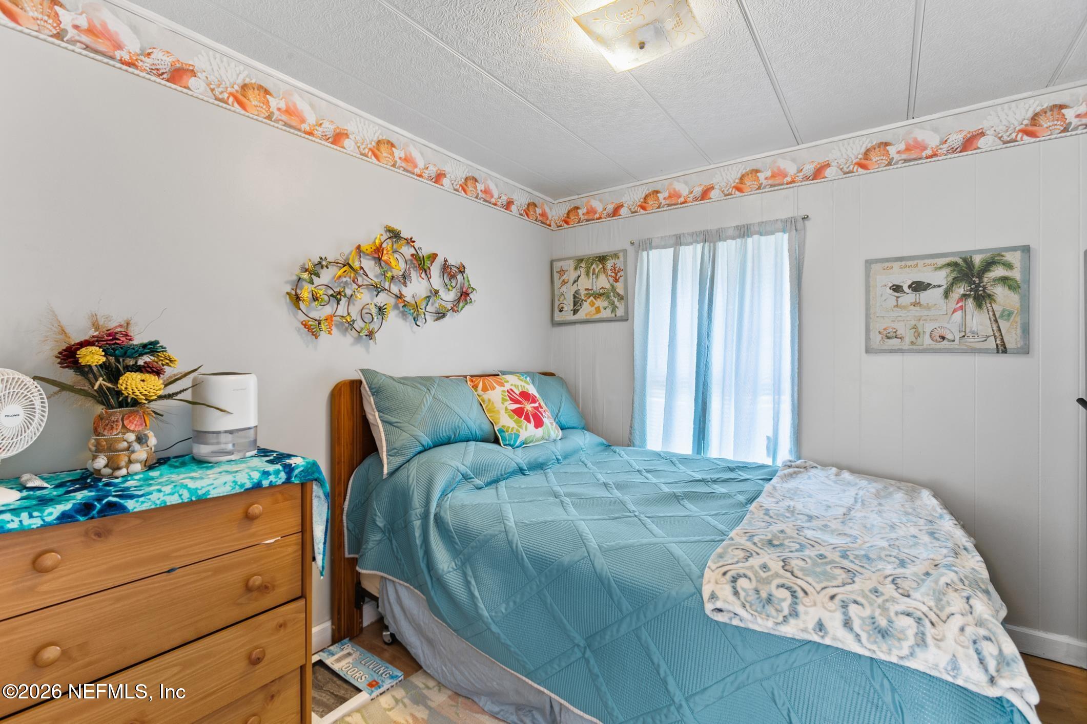 Bedroom with a blue-quilted bed, wooden dresser, and coastal decor.