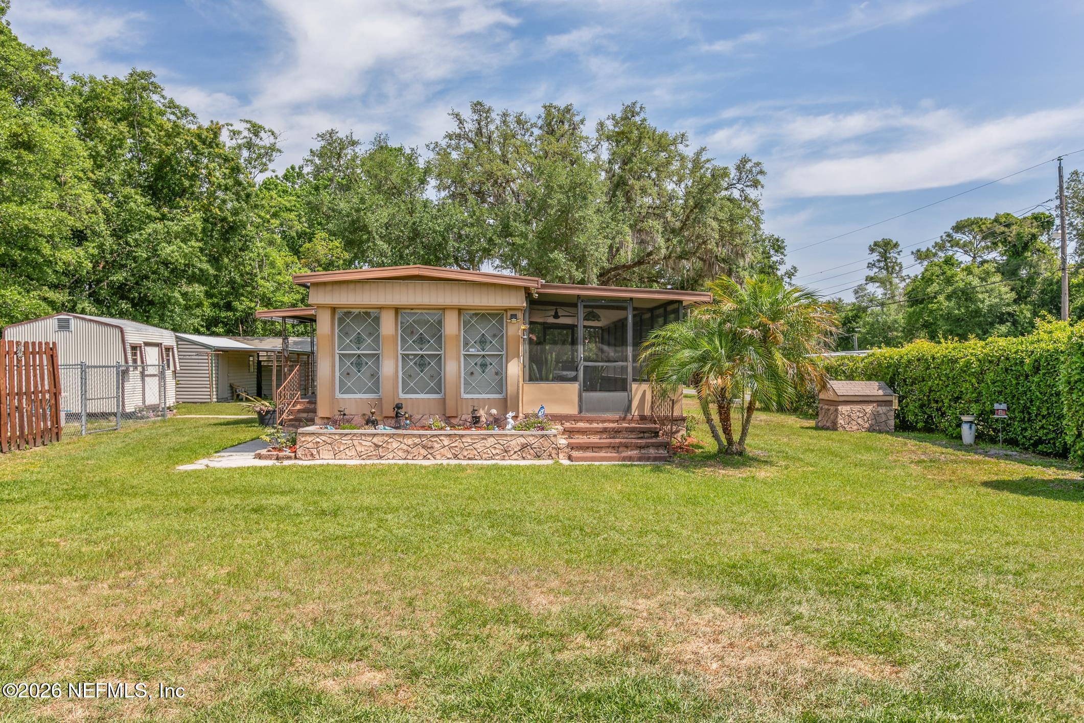 Tan home with a screened porch, front steps, and a broad lawn beneath mature trees.