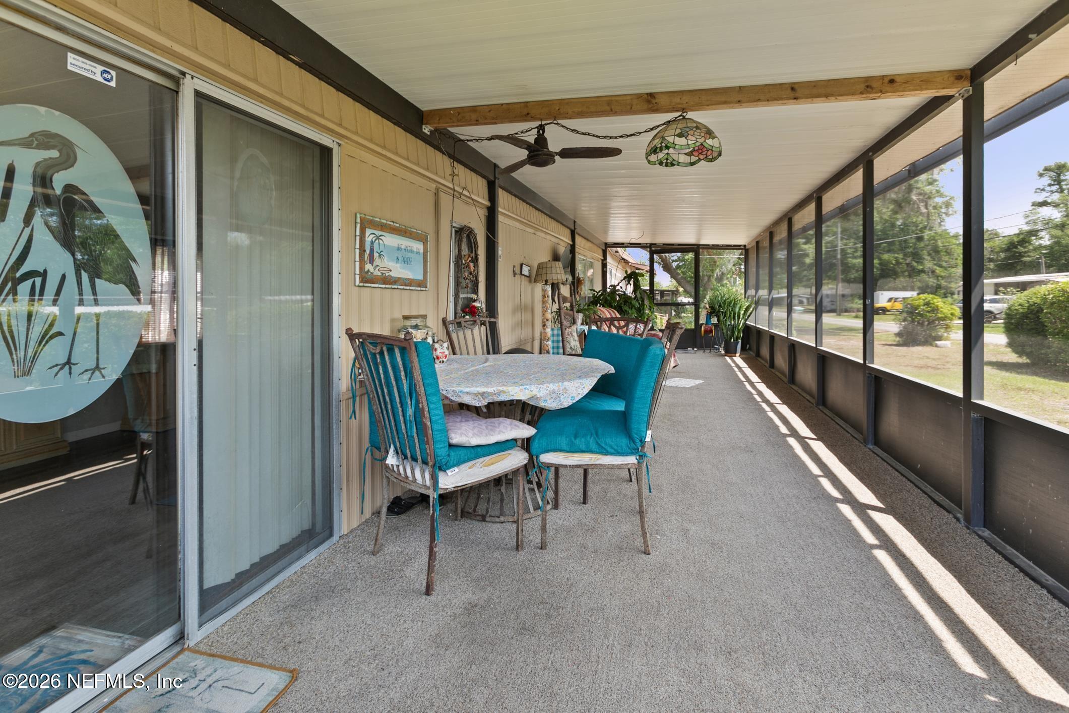 Screened-in porch with a dining set, turquoise cushions, potted plants, and a ceiling fan.