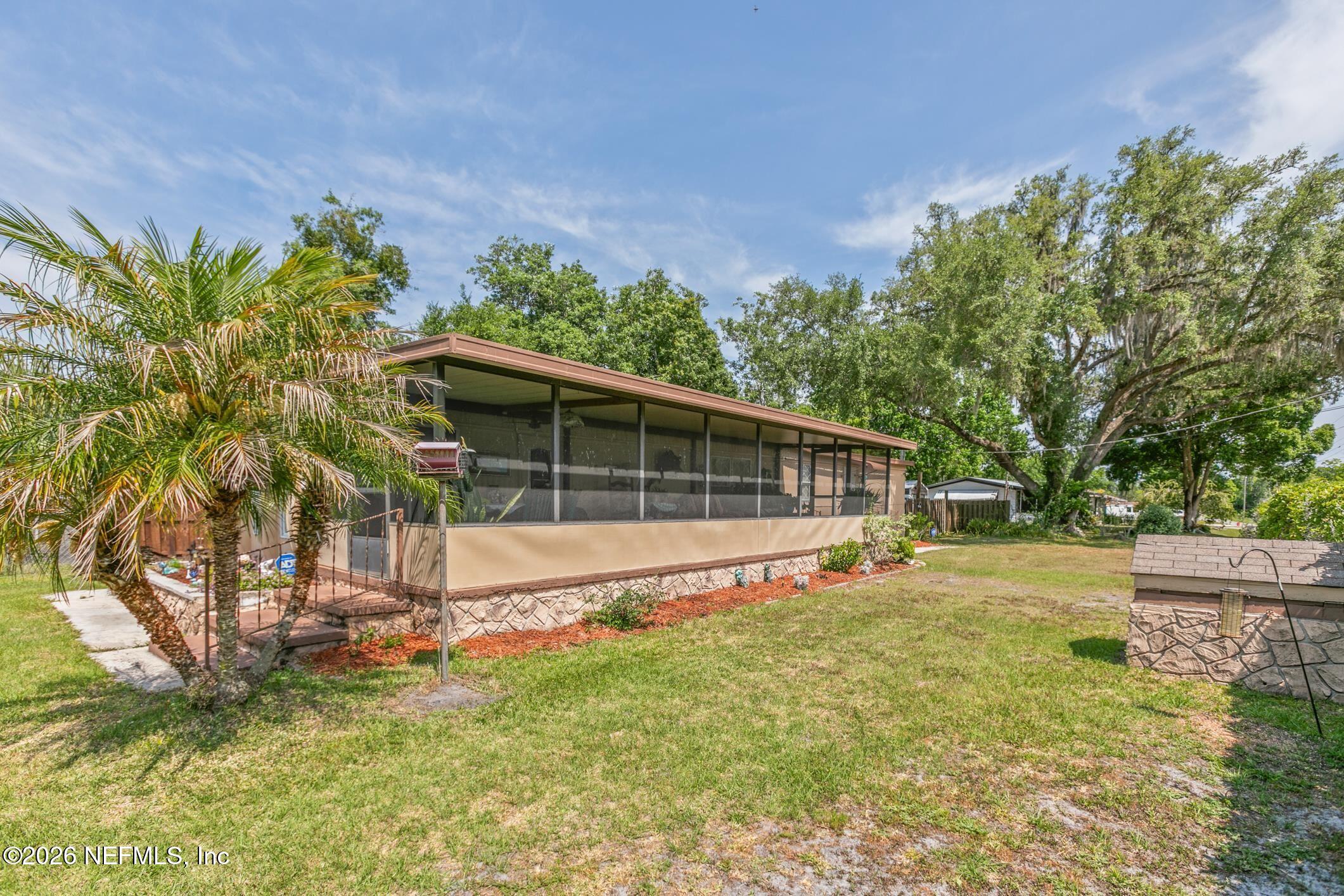 Single-story home with a long screened porch, palm trees, and a broad grassy yard.