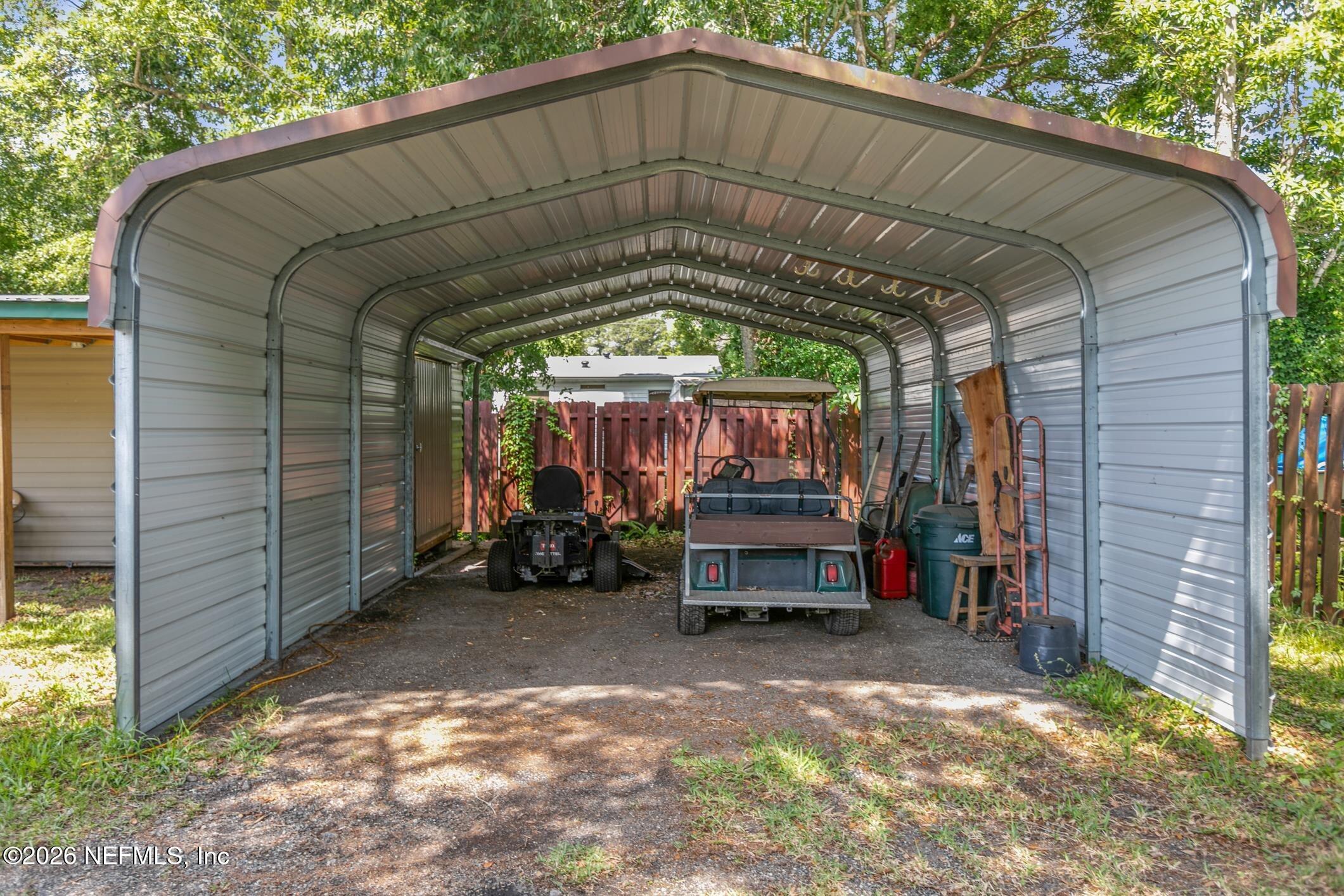 Metal carport sheltering two utility carts beside a fenced yard.