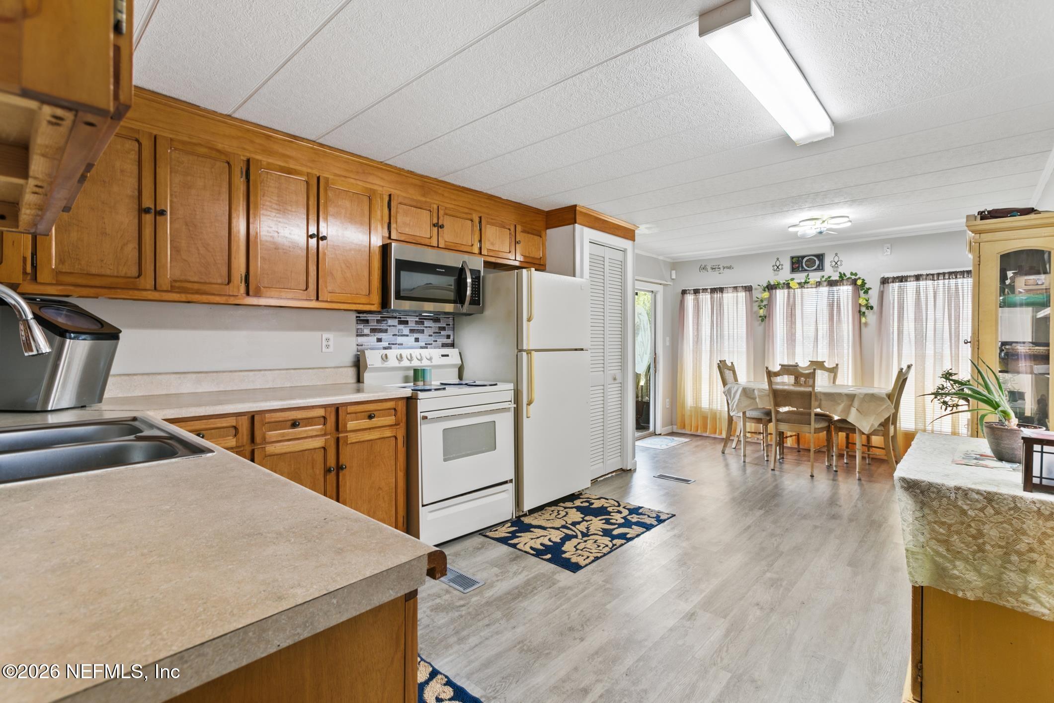 Kitchen with honey-toned cabinets and white appliances opening into a dining area.