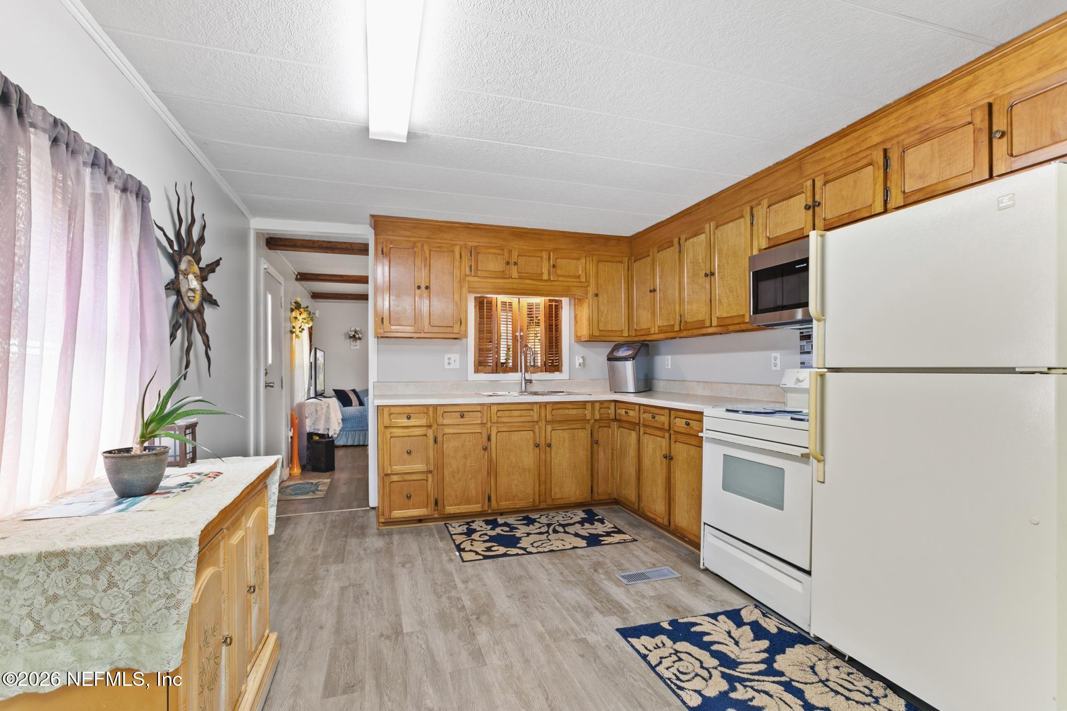 Kitchen with honey-toned wood cabinets, white appliances, and a shuttered window.