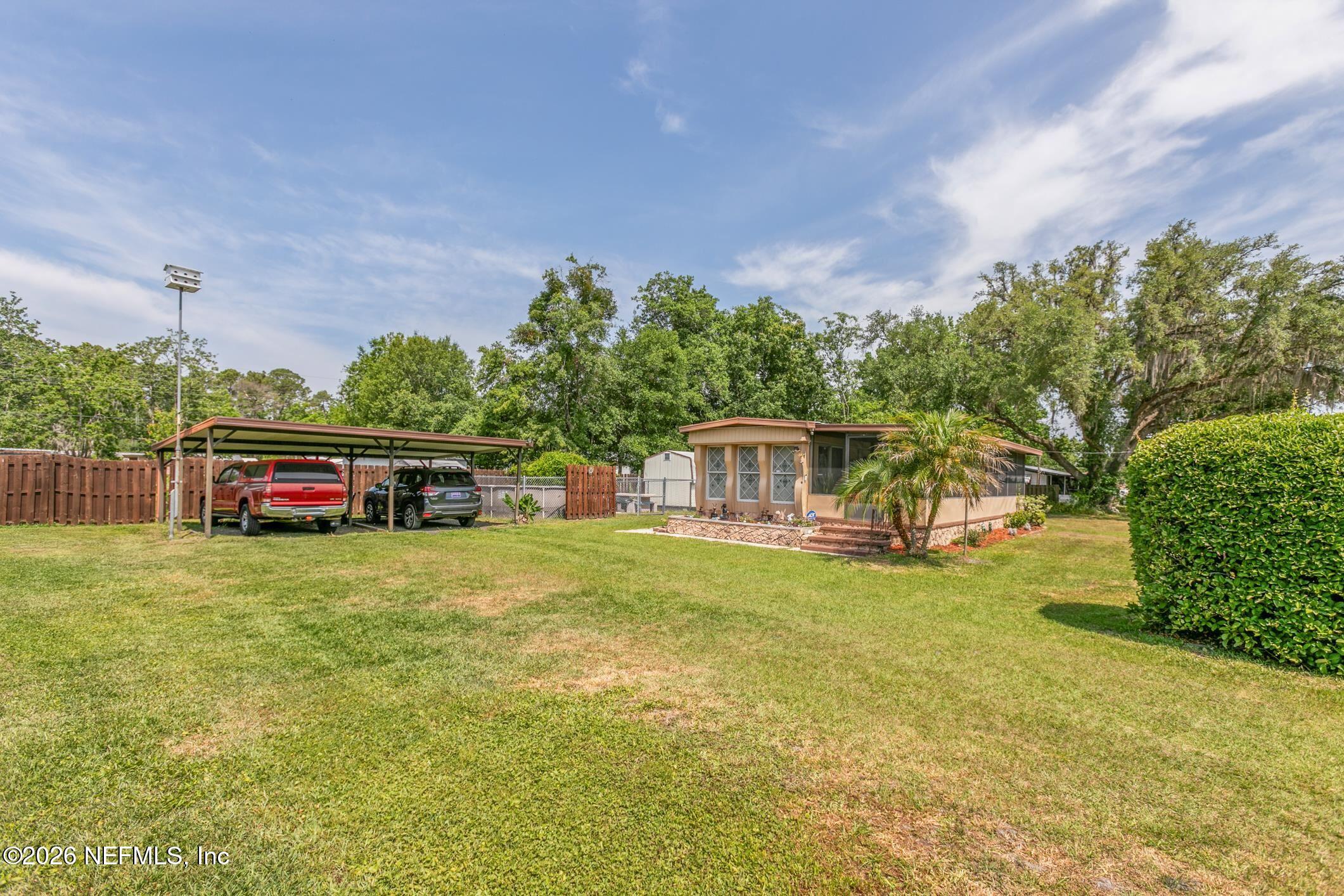 Single-story home beside a grassy yard, with a covered carport and mature trees.