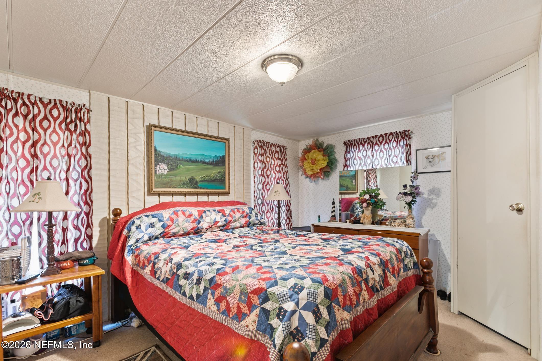 Bedroom with a colorful patchwork quilt on a wooden bed and red-and-white patterned curtains.
