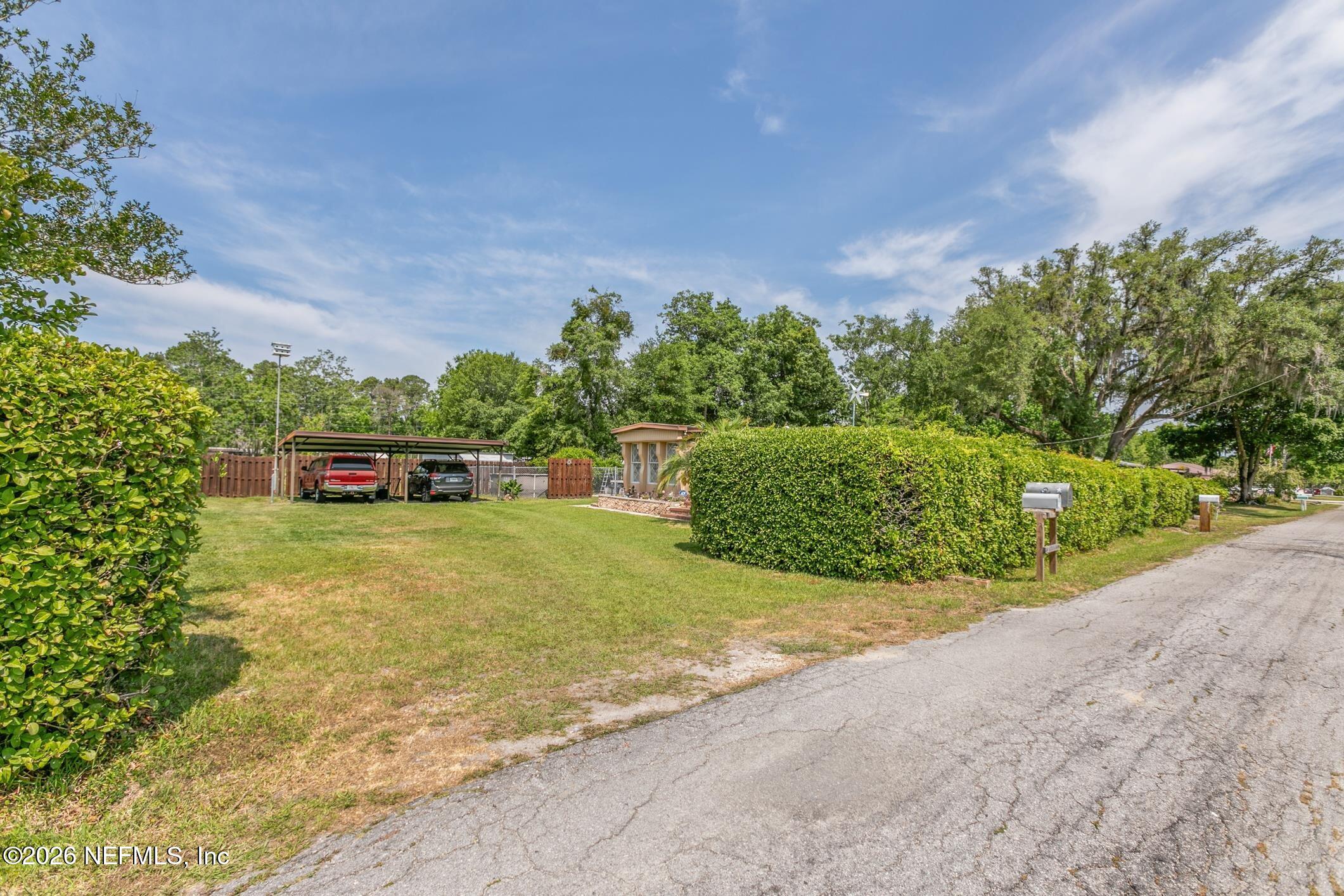 Property frontage with a grassy yard, tall hedges, a covered carport, and a small outbuilding.
