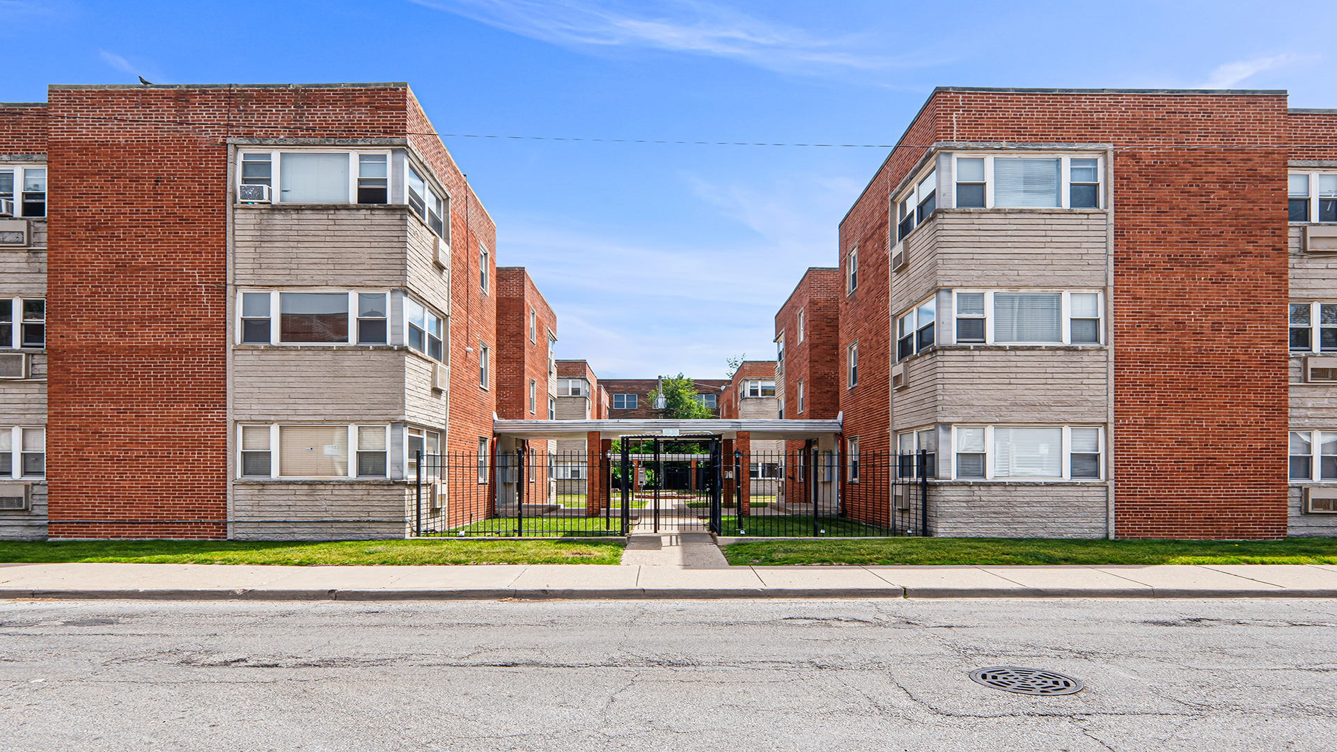 Multi-unit apartment building with red brick facades and a covered, gated entrance walkway.