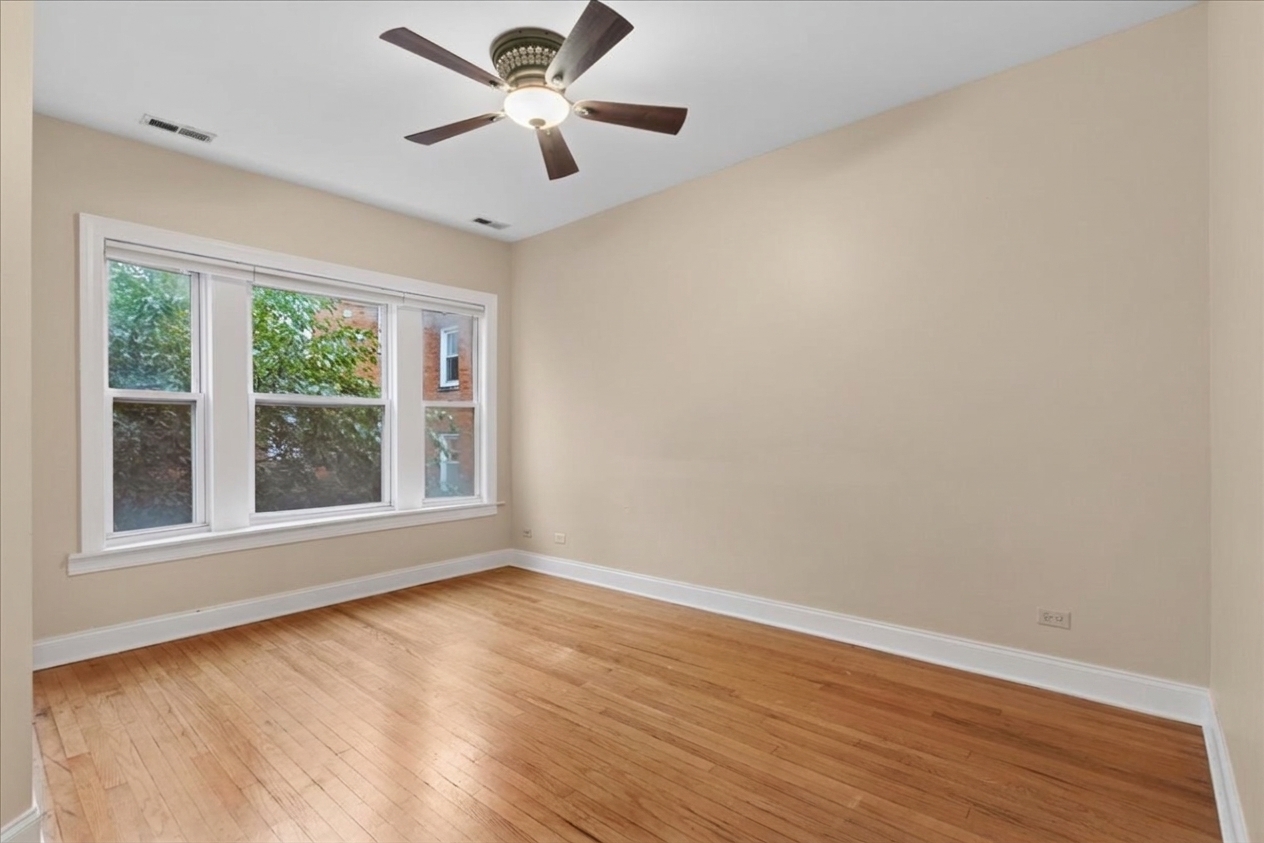 Empty room with hardwood floors, a ceiling fan, and wide windows.