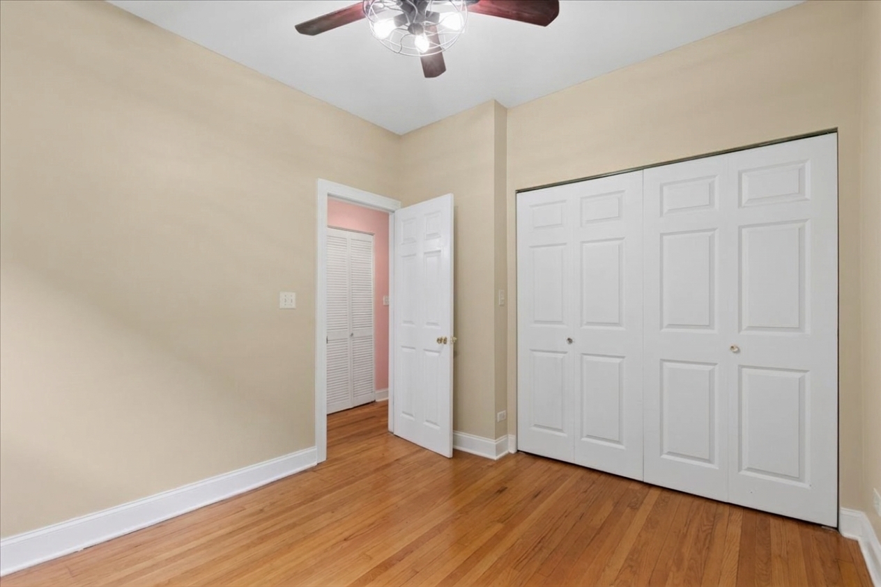 Empty bedroom with hardwood floors, a ceiling fan, and white double closet doors.