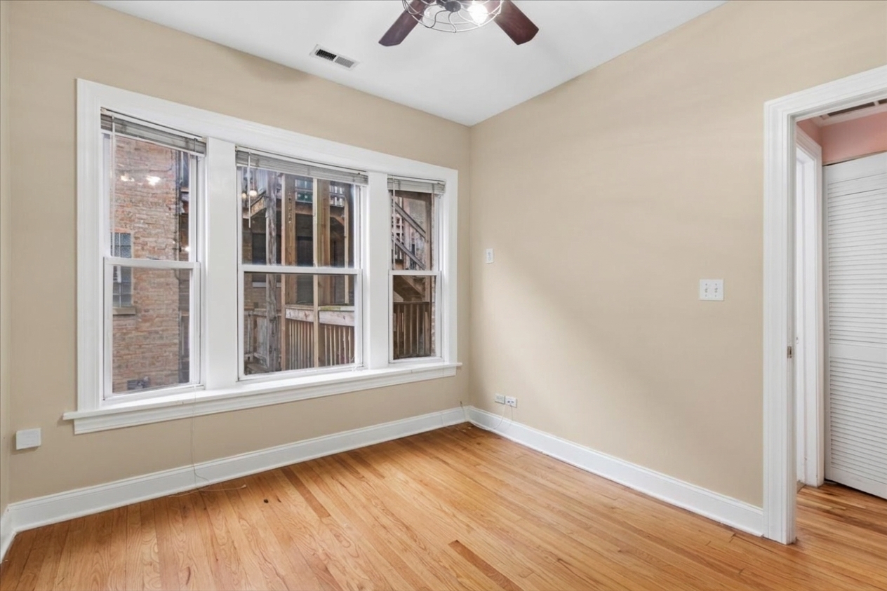 Empty room with hardwood floors, three windows, and a ceiling fan.
