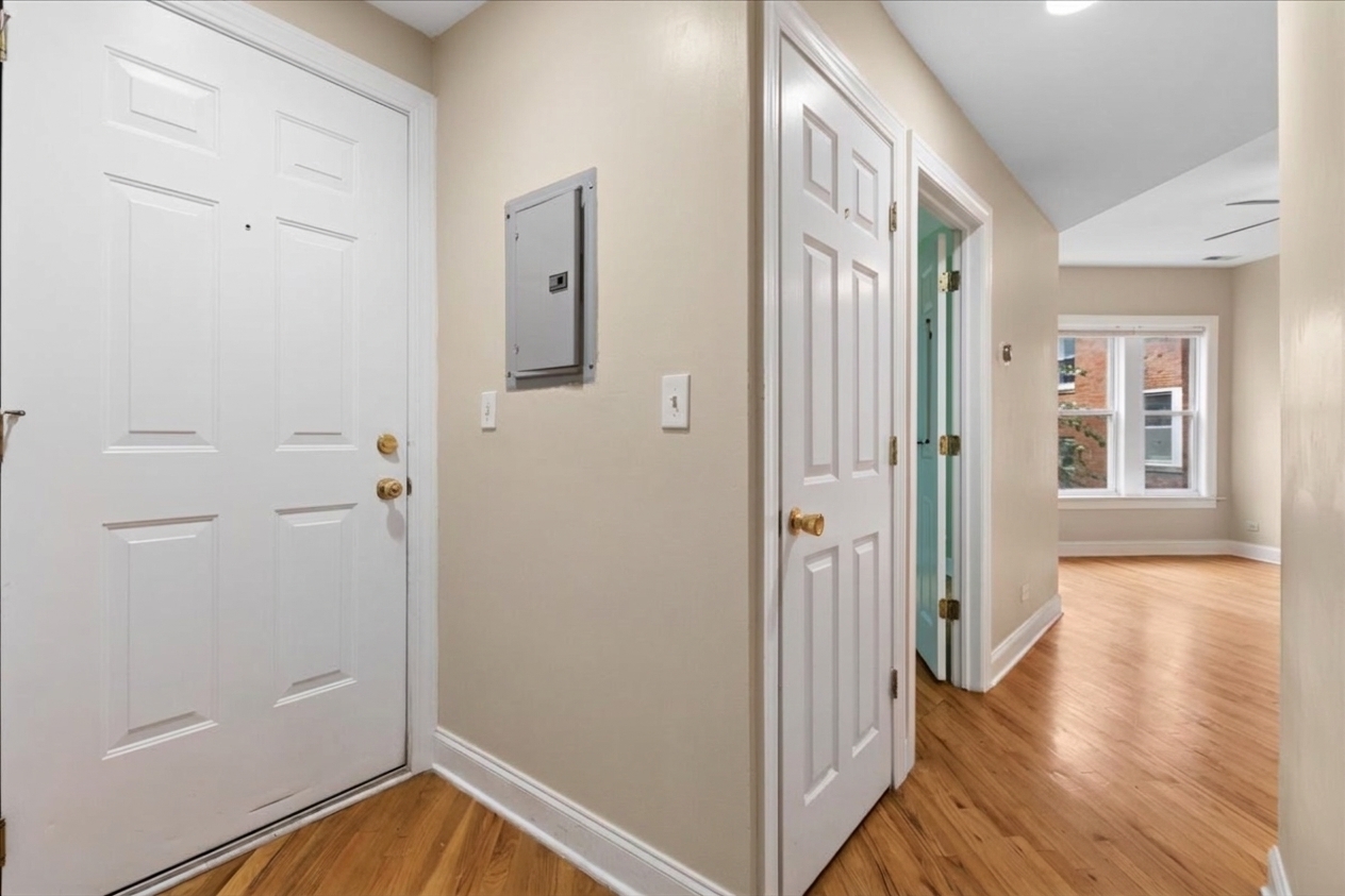 Apartment entry hall with hardwood floors and a hallway leading to a bright windowed room.