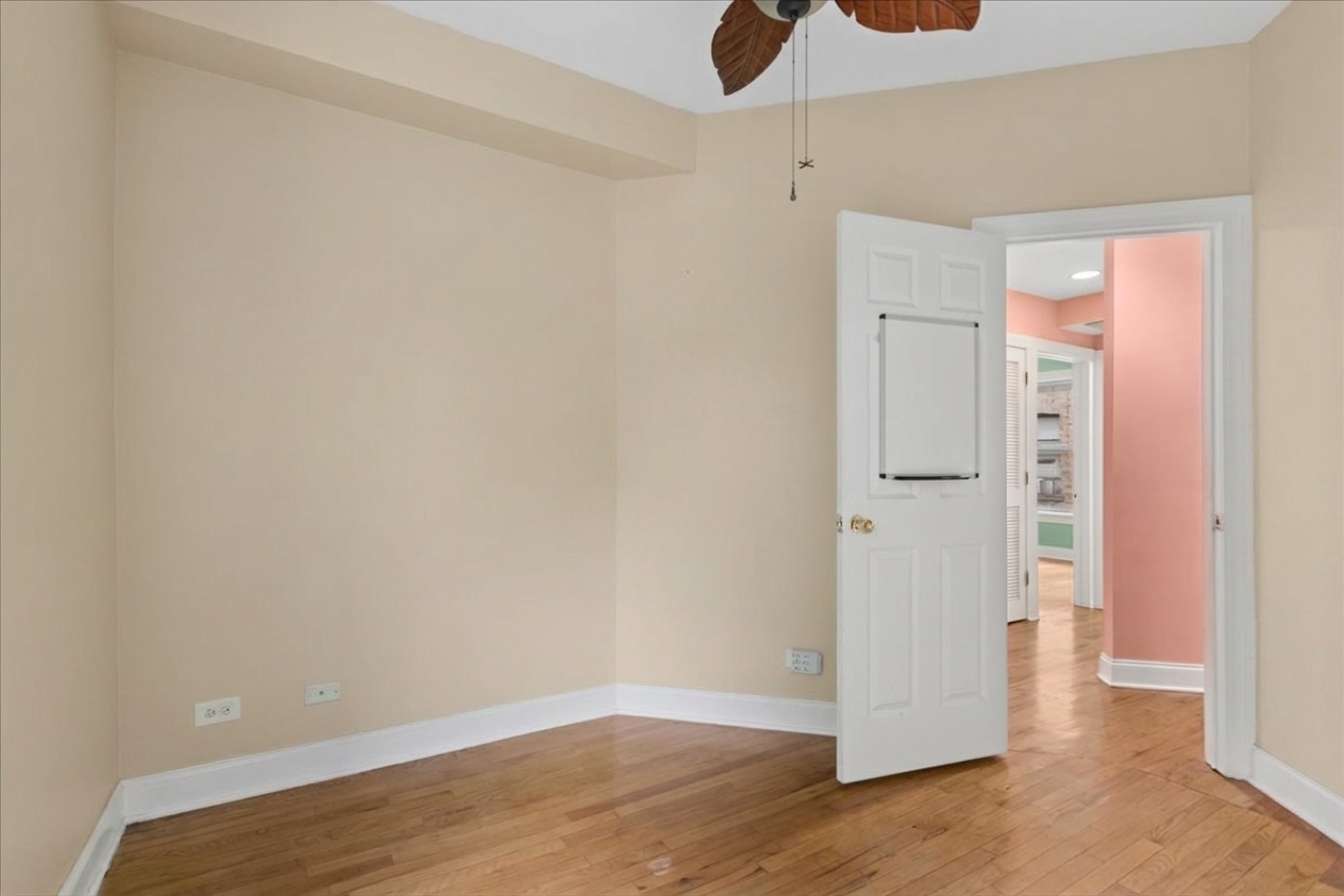 Empty bedroom with hardwood floors, a ceiling fan, and an open door to a coral hallway.