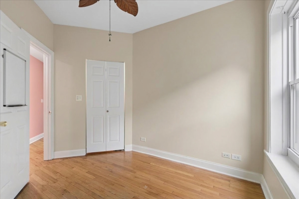 Empty bedroom with hardwood floors, a white closet, and tall windows.