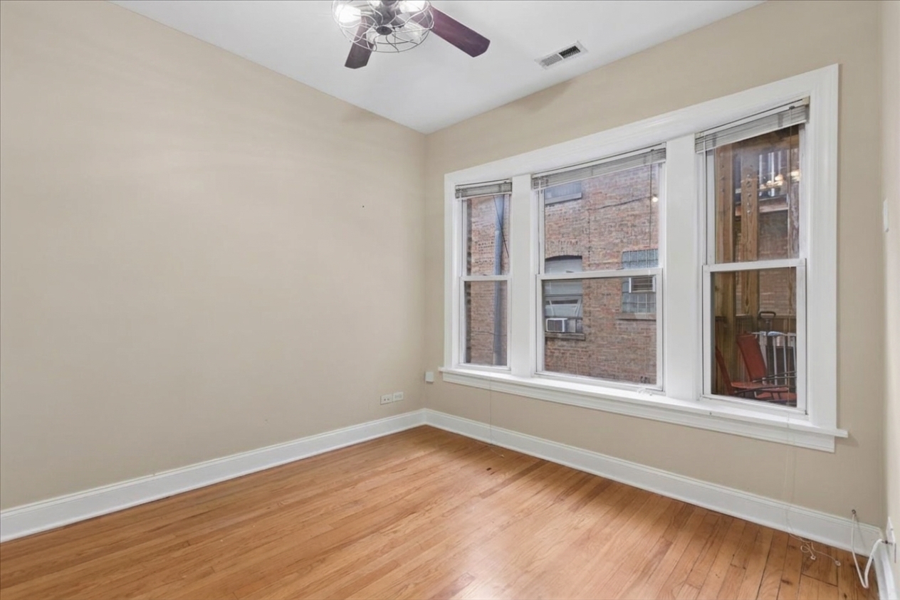 Empty room with hardwood floors, a ceiling fan, and three large windows.