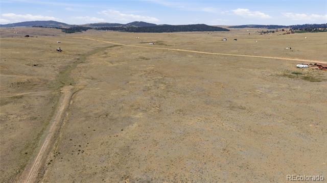 Aerial view of open grassland with a dirt track and distant hills.