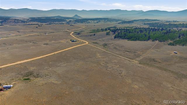 Aerial view of open rural land crossed by a winding dirt road, with mountains beyond.