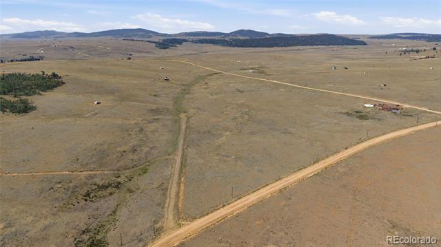Aerial view of open dry grassland crossed by dirt roads, with scattered structures and distant low hills.