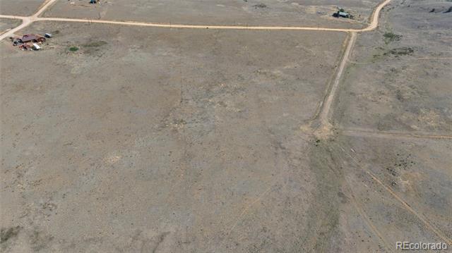 Aerial view of a dry open parcel crossed by faint tracks, with dirt roads and distant buildings.