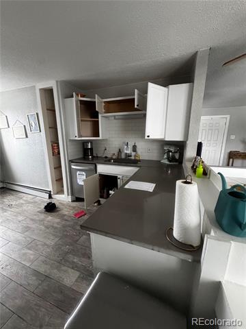 Kitchen with open white cabinets, gray countertops, and a peninsula holding a paper towel roll and teal containers.