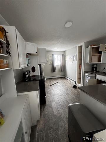 Narrow kitchen with white cabinets, dark counters, and gray wood-look flooring leading to a curtained window.