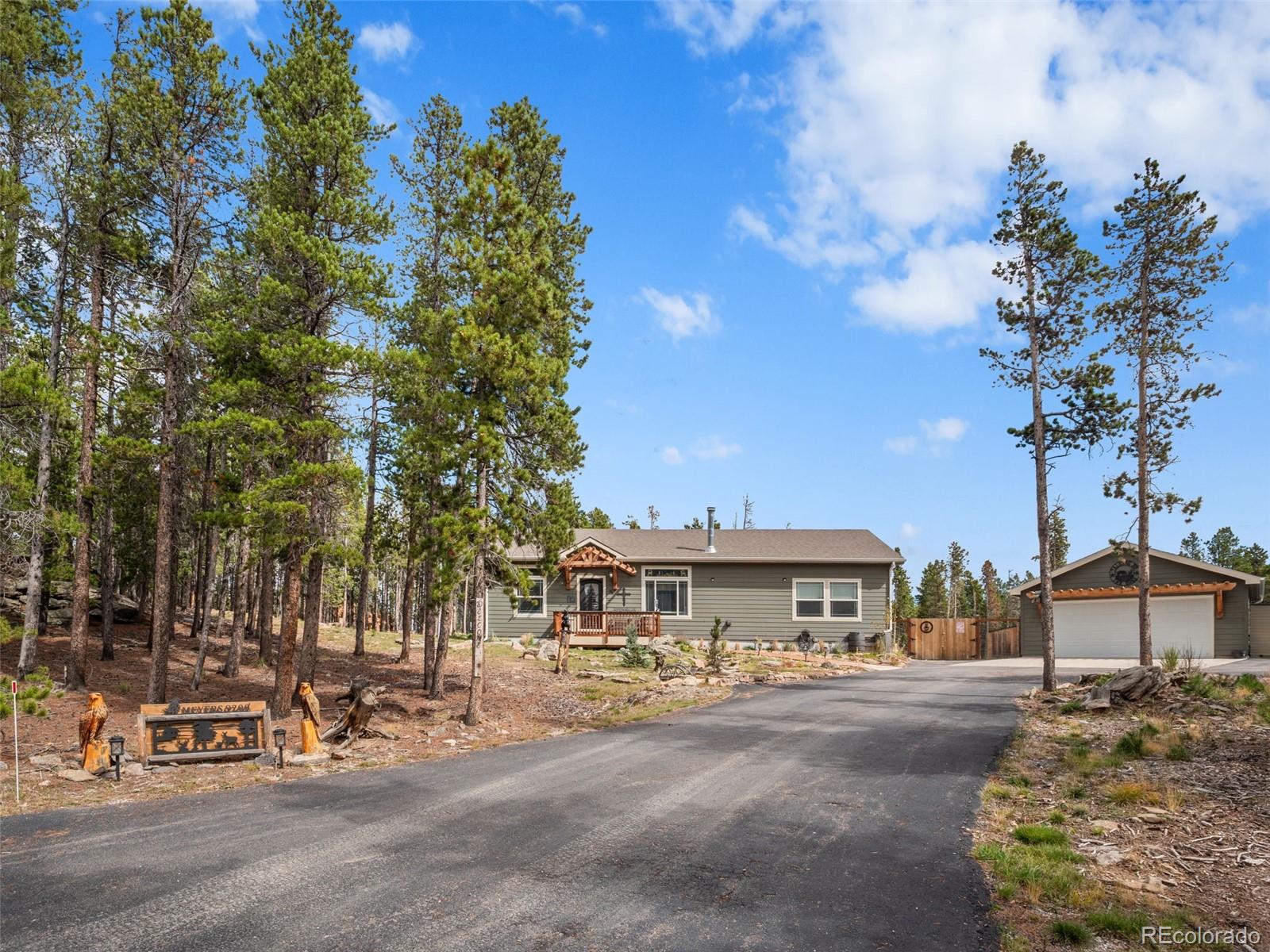 Gray single-story home and detached garage among pine trees, viewed from the driveway.
