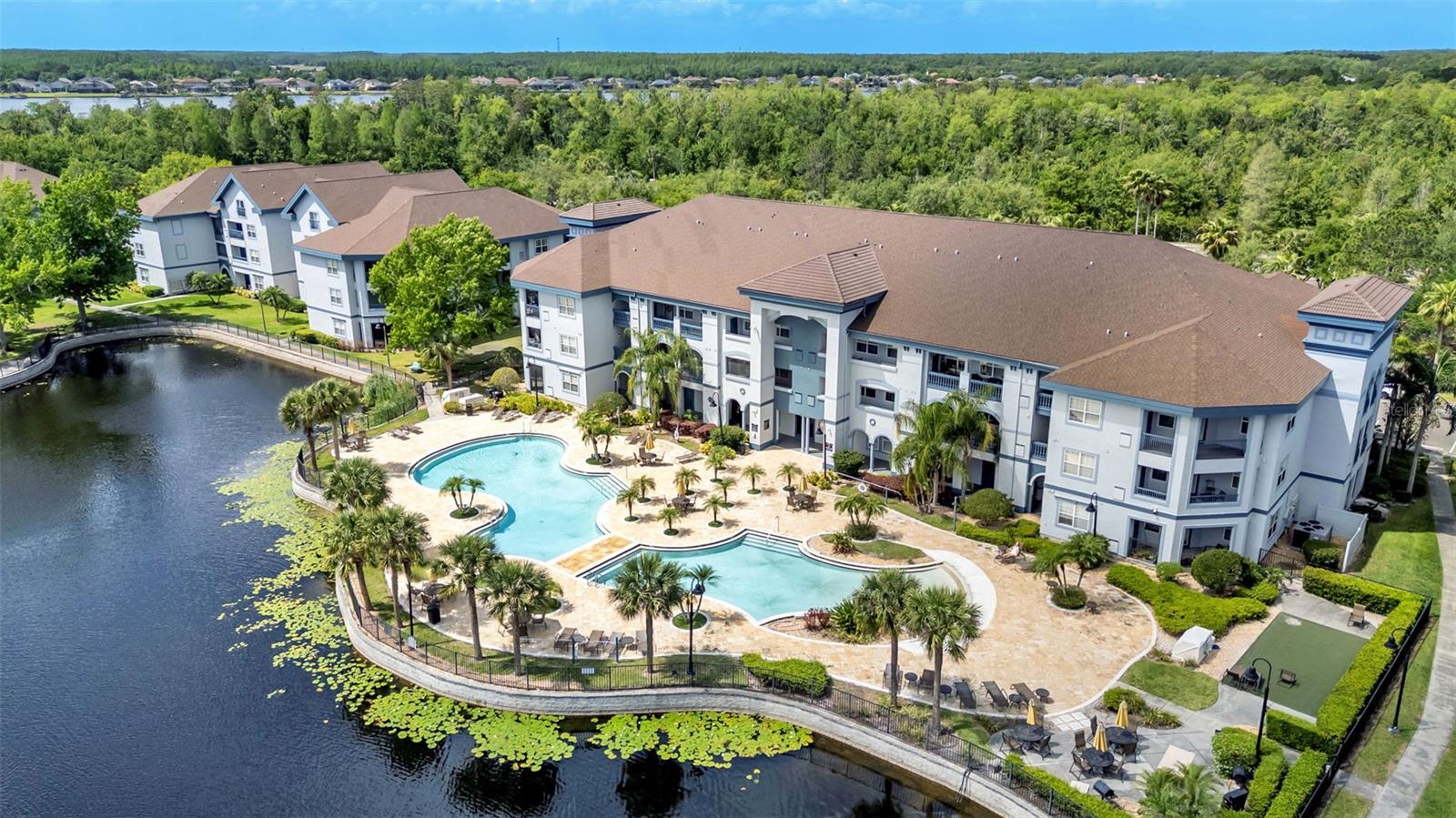 Aerial view of condominiums with two pools beside a pond.