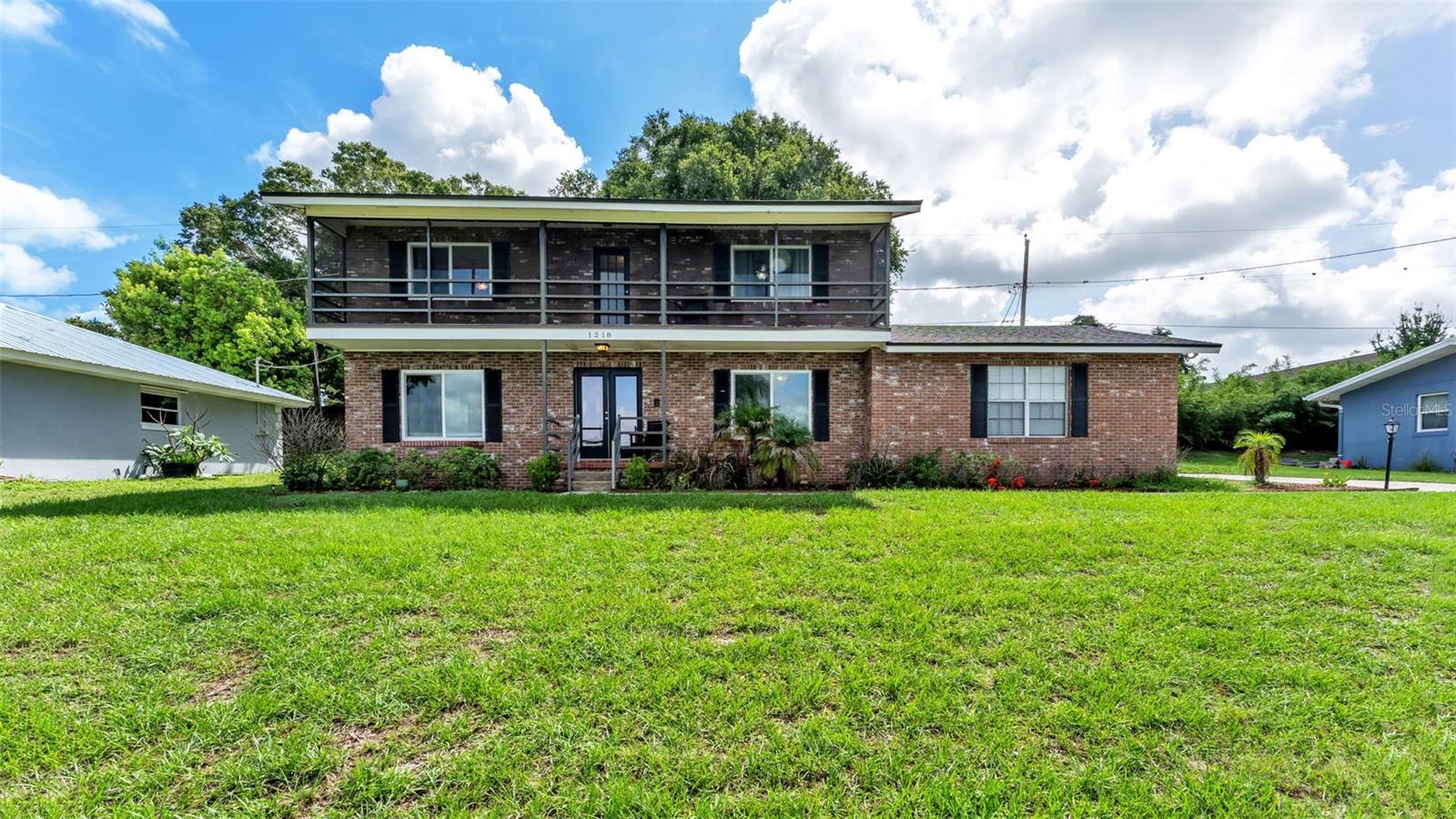 Two-story brick home with a long upper balcony and broad front lawn.