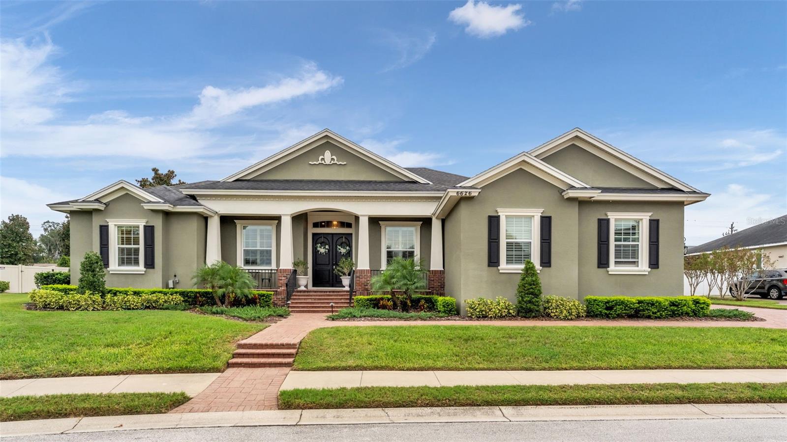 Single-story olive-gray home with multiple gables, black shutters, and a brick walkway through the front lawn.