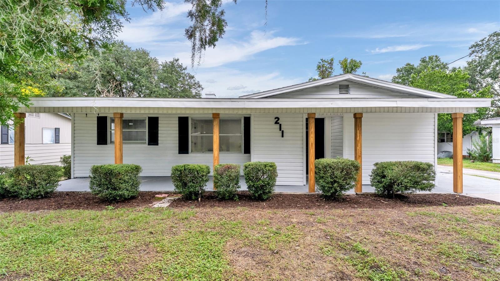 Single-story white house with a broad covered porch, wood posts, black shutters, and front shrubs.