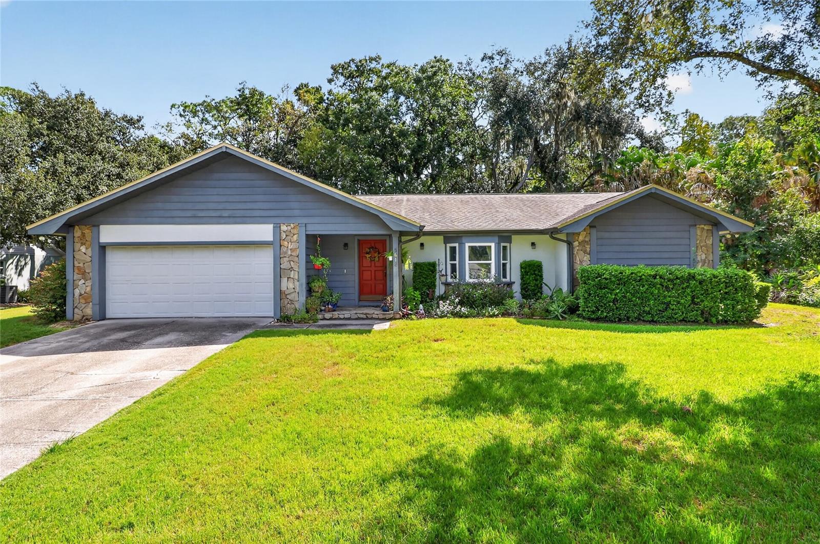 Single-story gray house with stone accents, a red front door, and a broad green lawn.
