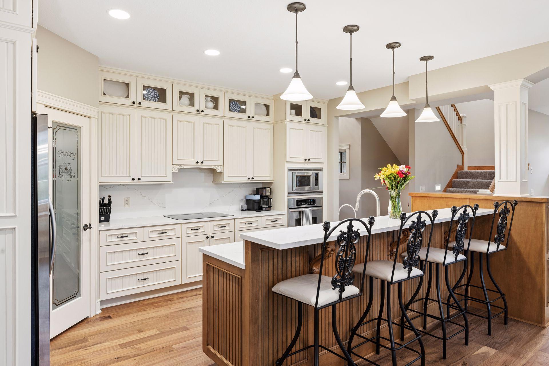 Kitchen with white cabinetry, a wood-paneled island, ornate black stools, and stainless steel appliances.