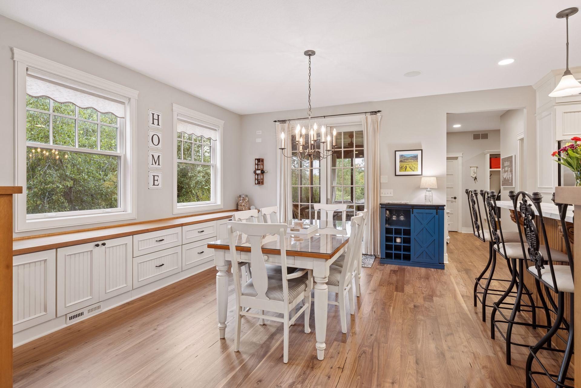 Dining room with white built-in cabinetry, large windows, a chandelier, and an adjoining kitchen with a blue island.