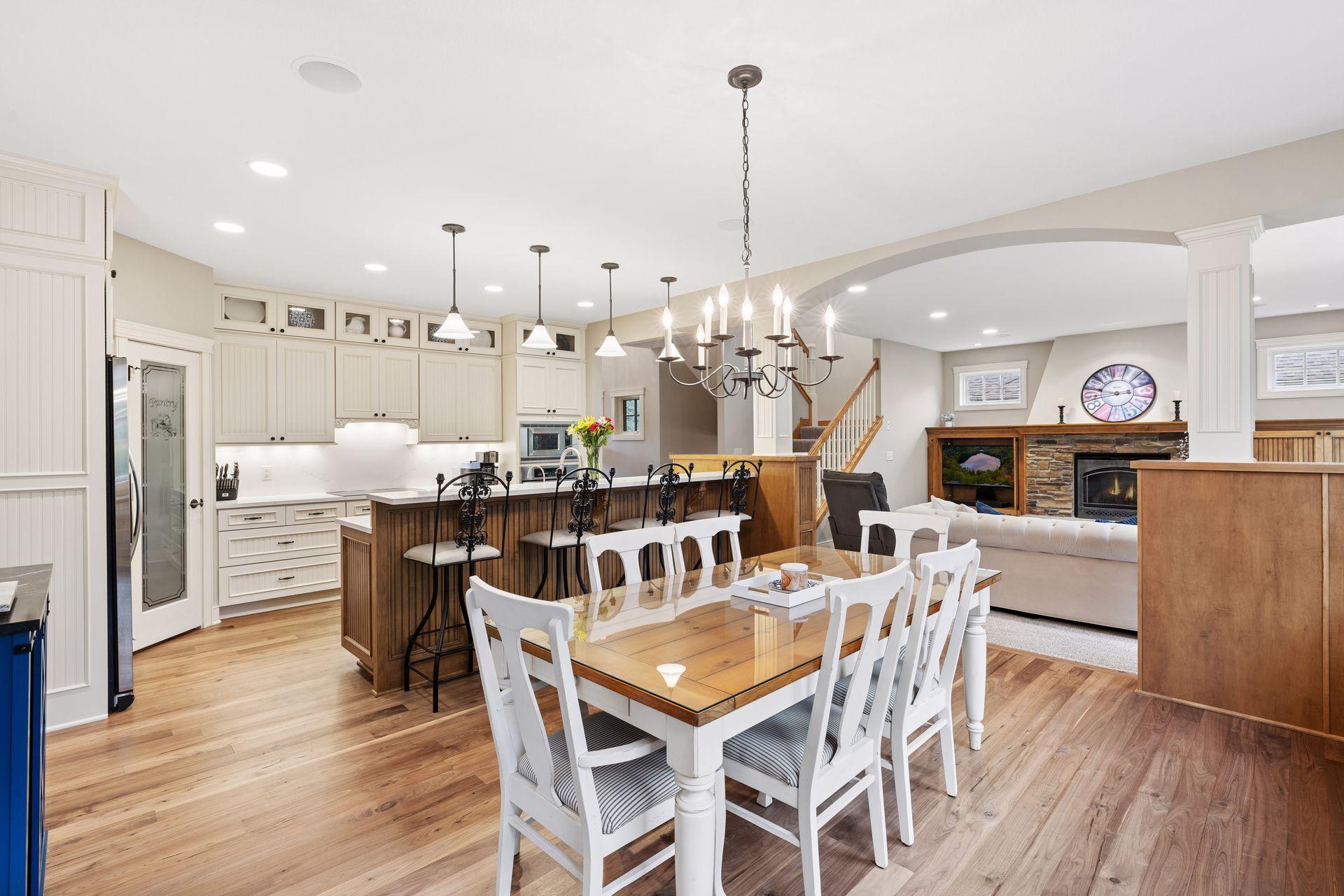 Open kitchen and dining area with white cabinets, a dark wood island, hardwood floors, and an adjoining fireplace living room.