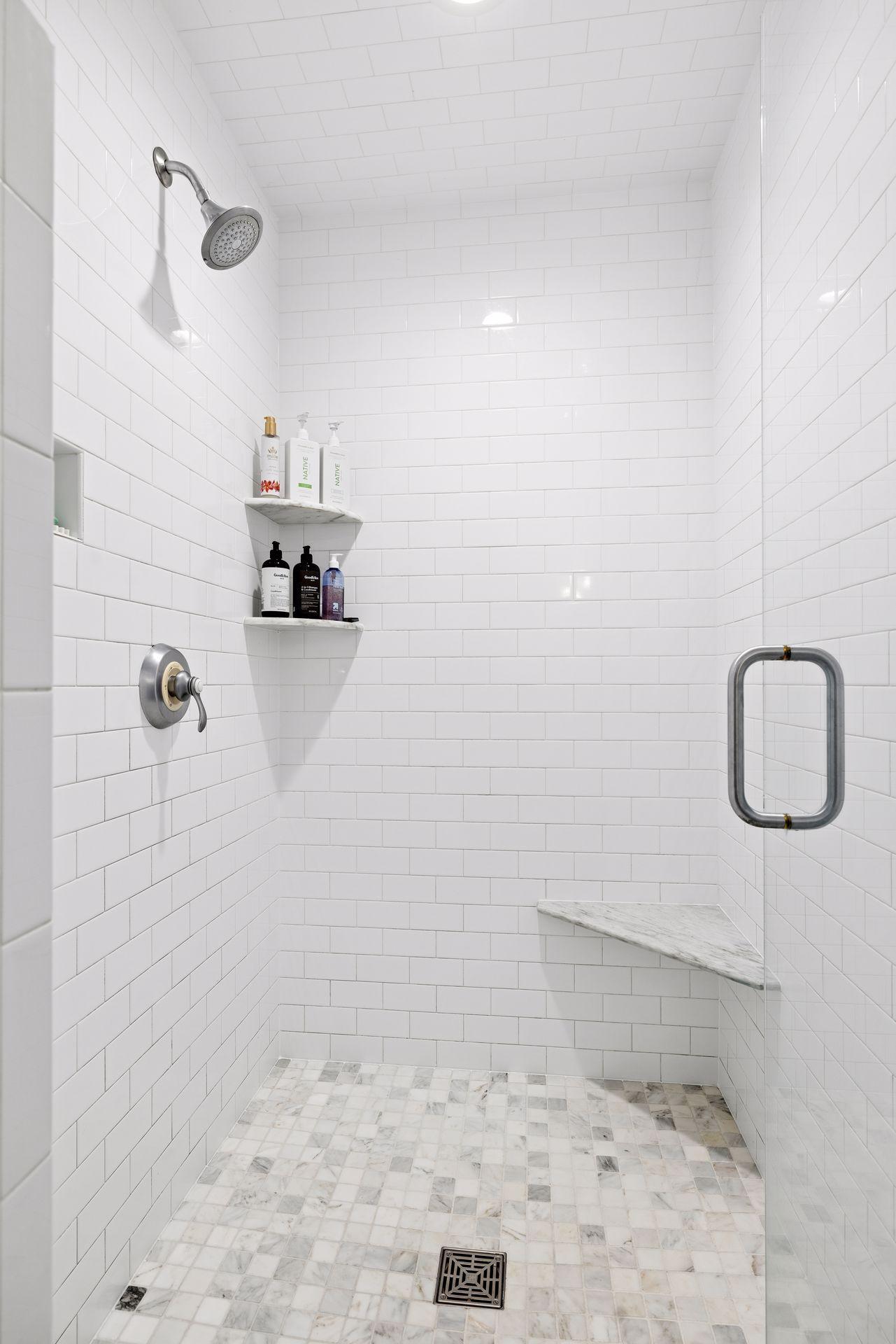 Walk-in shower with white subway tile, a marble mosaic floor, and a built-in marble bench.