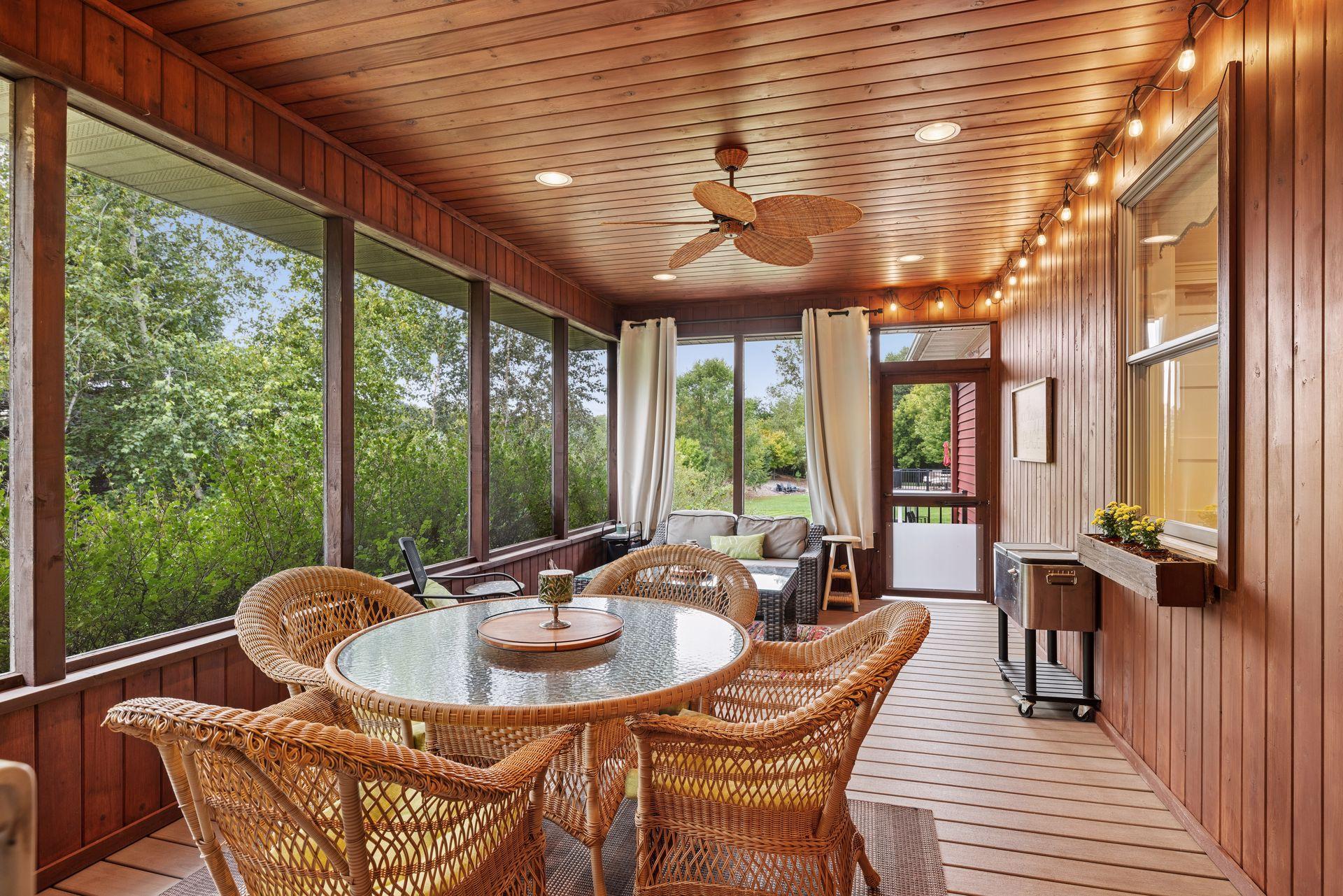 Wood-paneled sunroom with wicker seating, screened windows, and views of leafy trees.